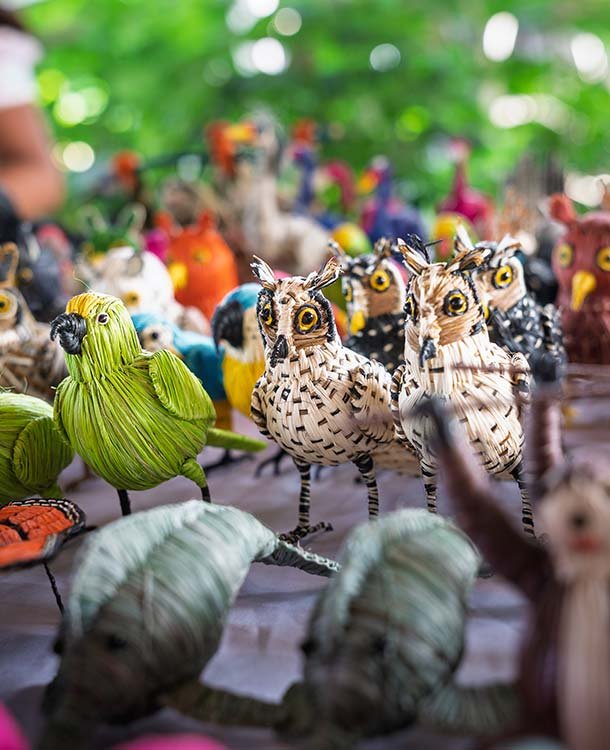 Colorful handcrafted animal figurines including birds, owls, and other creatures displayed on a table with a blurred outdoor background.