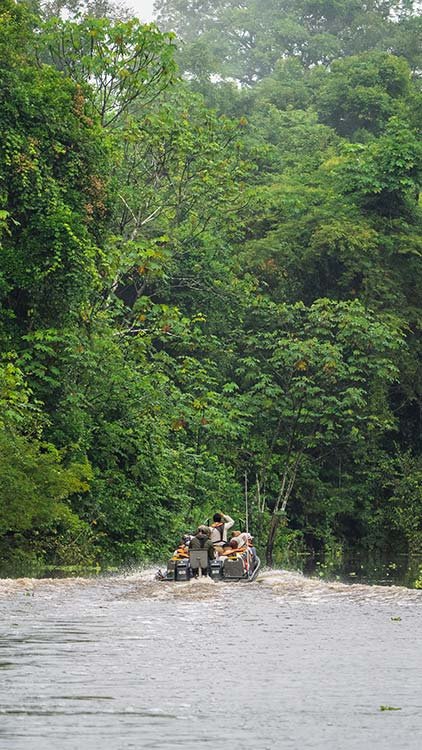 People riding in a boat on a river surrounded by dense green trees.