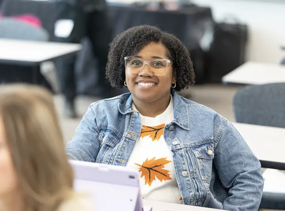 Black female sitting at a desk wearing glasses and smiling