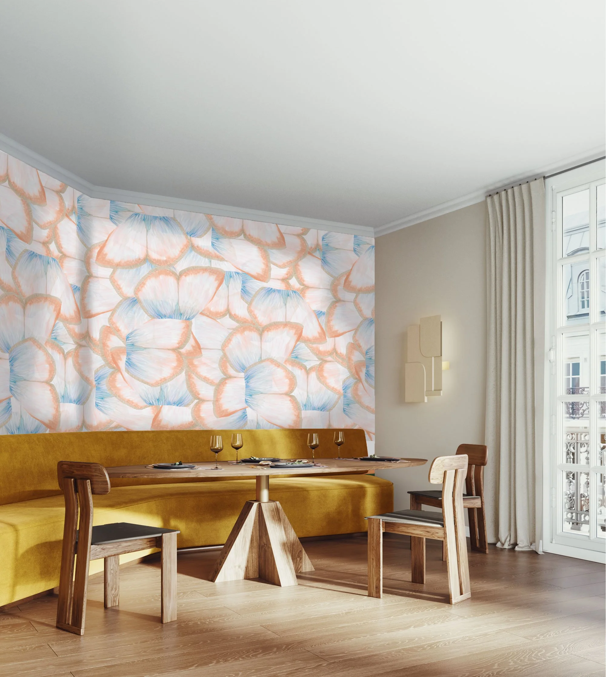 Dining room with a yellow velvet banquette, a wooden table set with glasses and plates, surrounded by wooden chairs, a floral wallpaper with large peach-colored petals, white walls, and a large window with cream curtains.