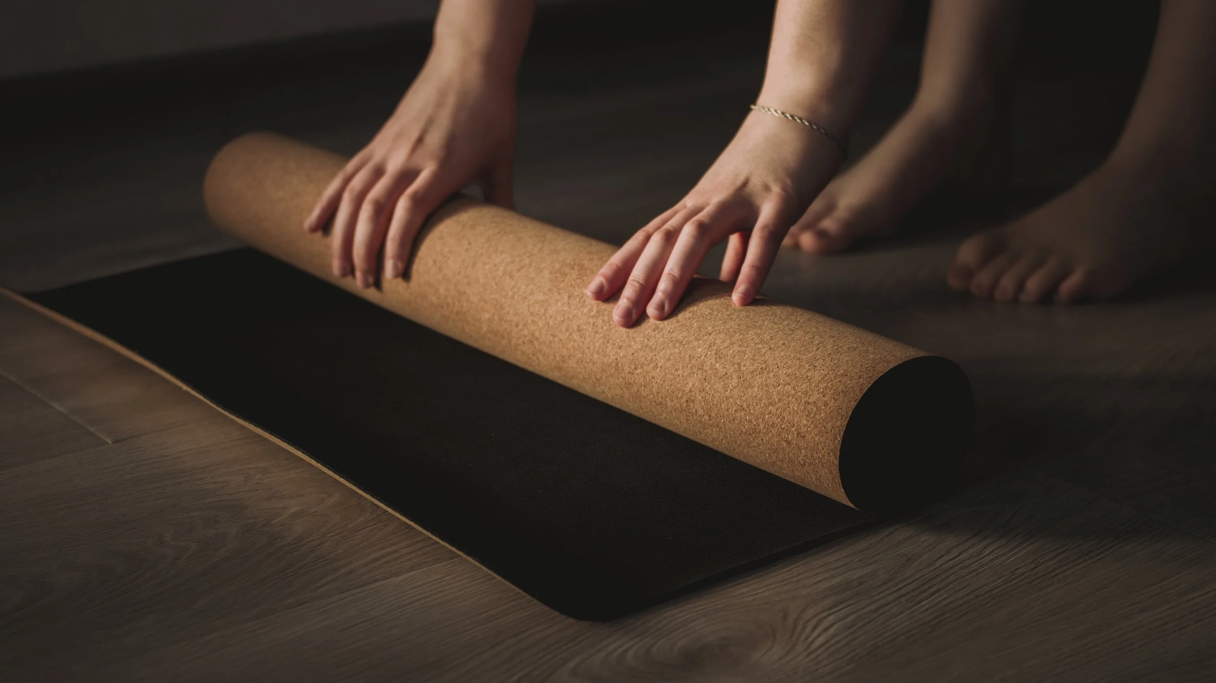 Person unrolling a yoga mat on a wooden floor.