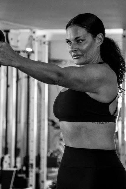 A woman lifting weights at the gym in black workout attire.