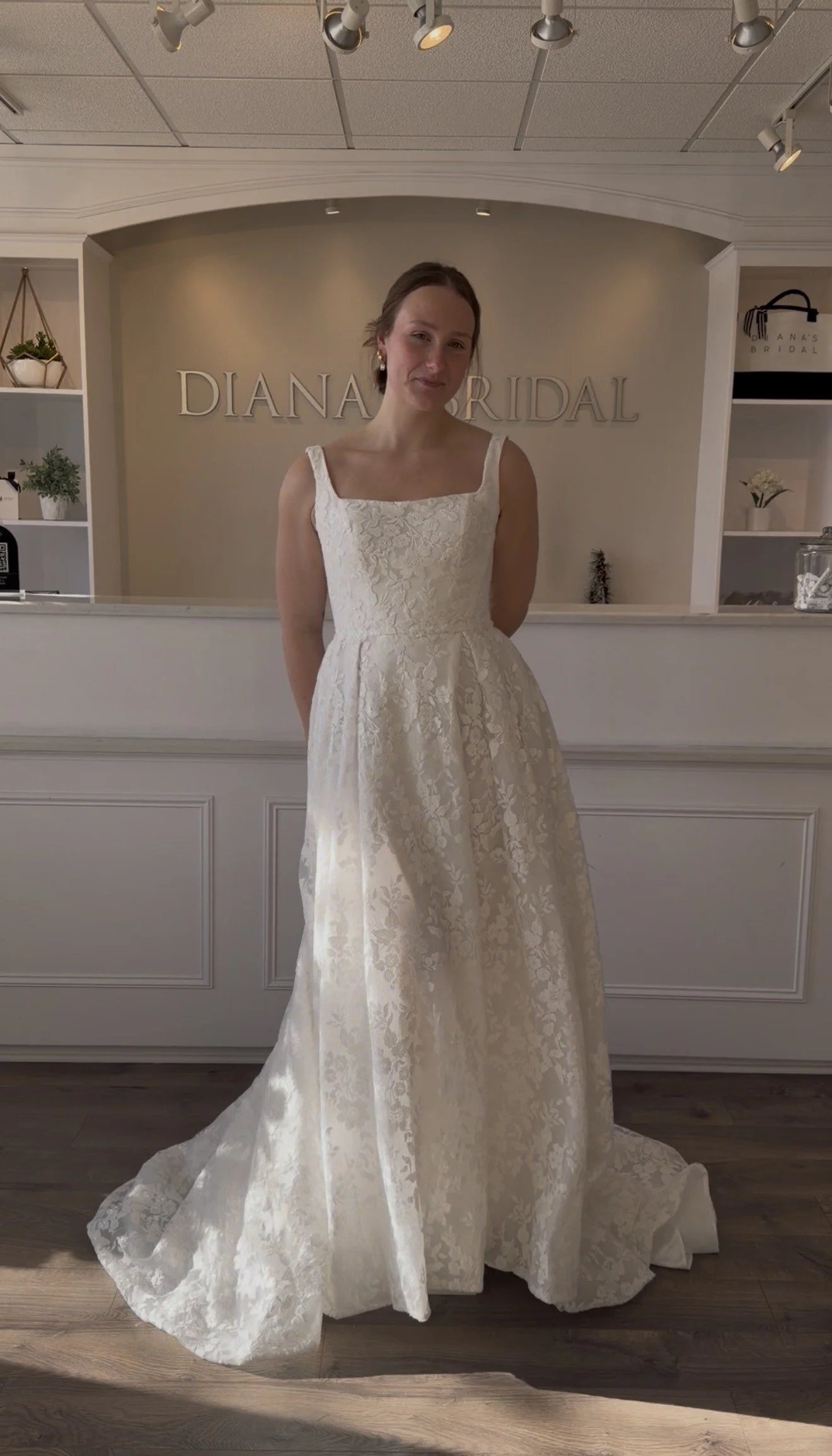 A woman trying on a white lace wedding dress in a bridal boutique.