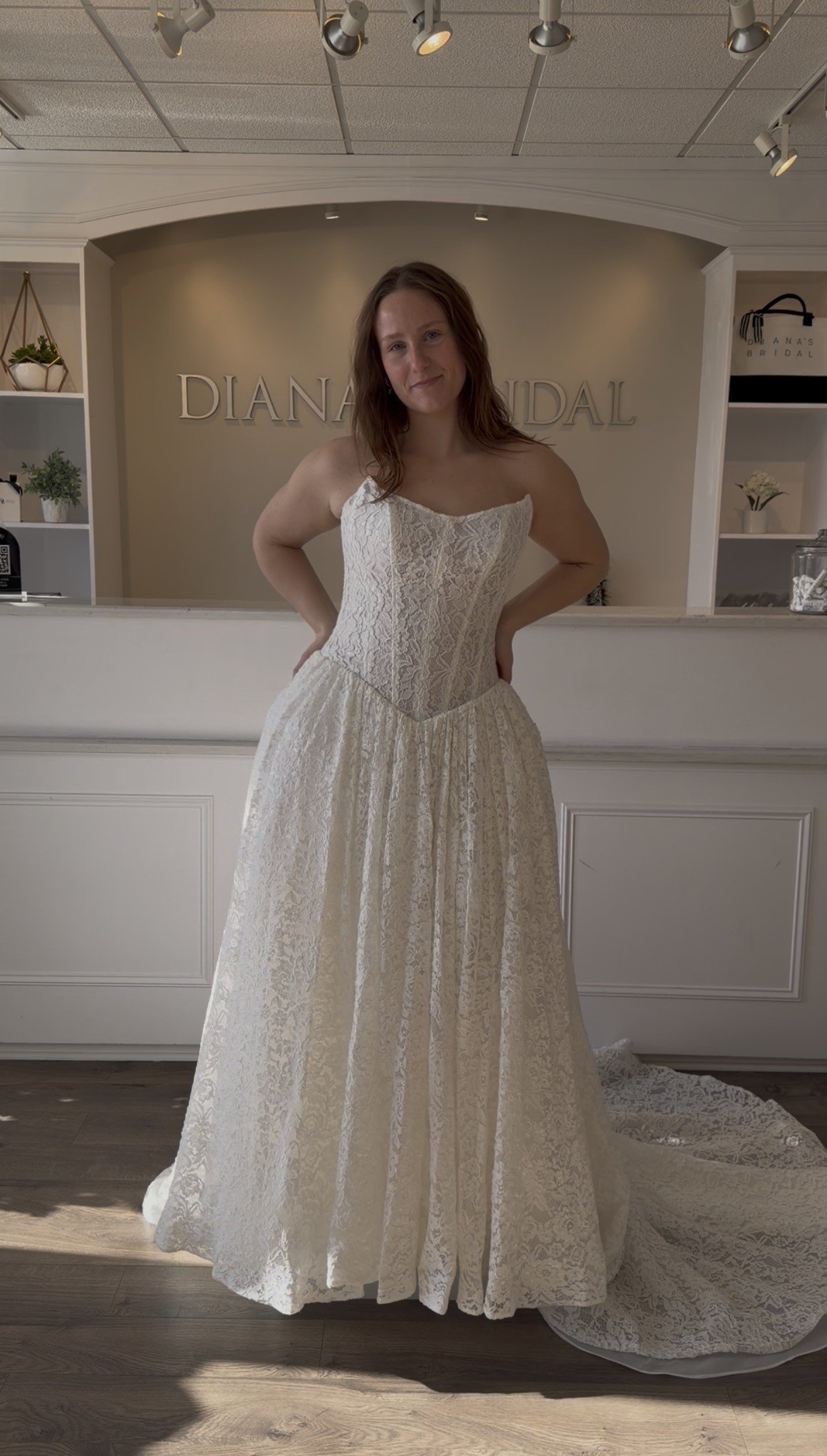 Woman inside a bridal shop trying on a white lace wedding dress with a sweetheart neckline.
