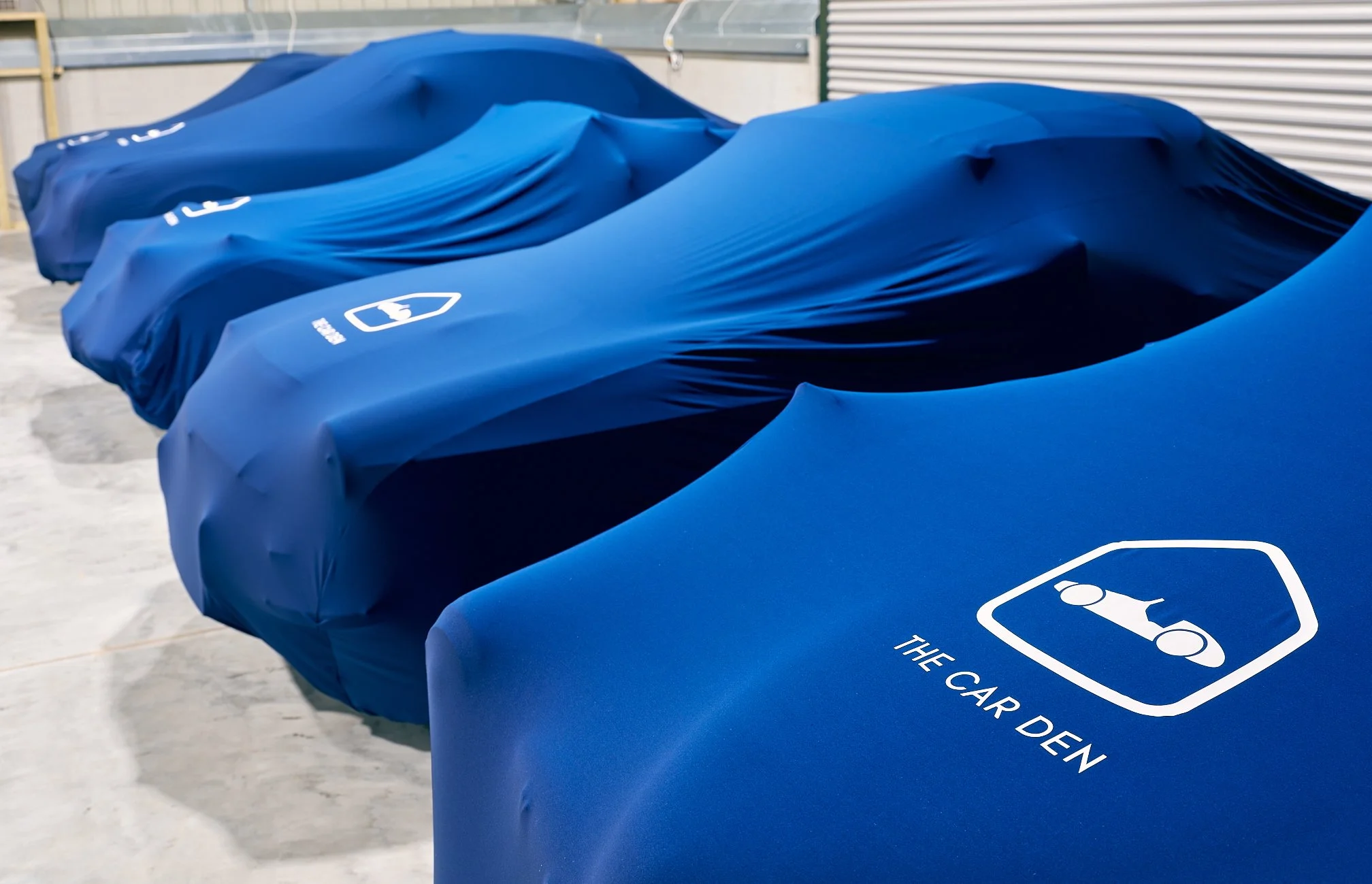 Row of classic cars under branded The Car Den covers