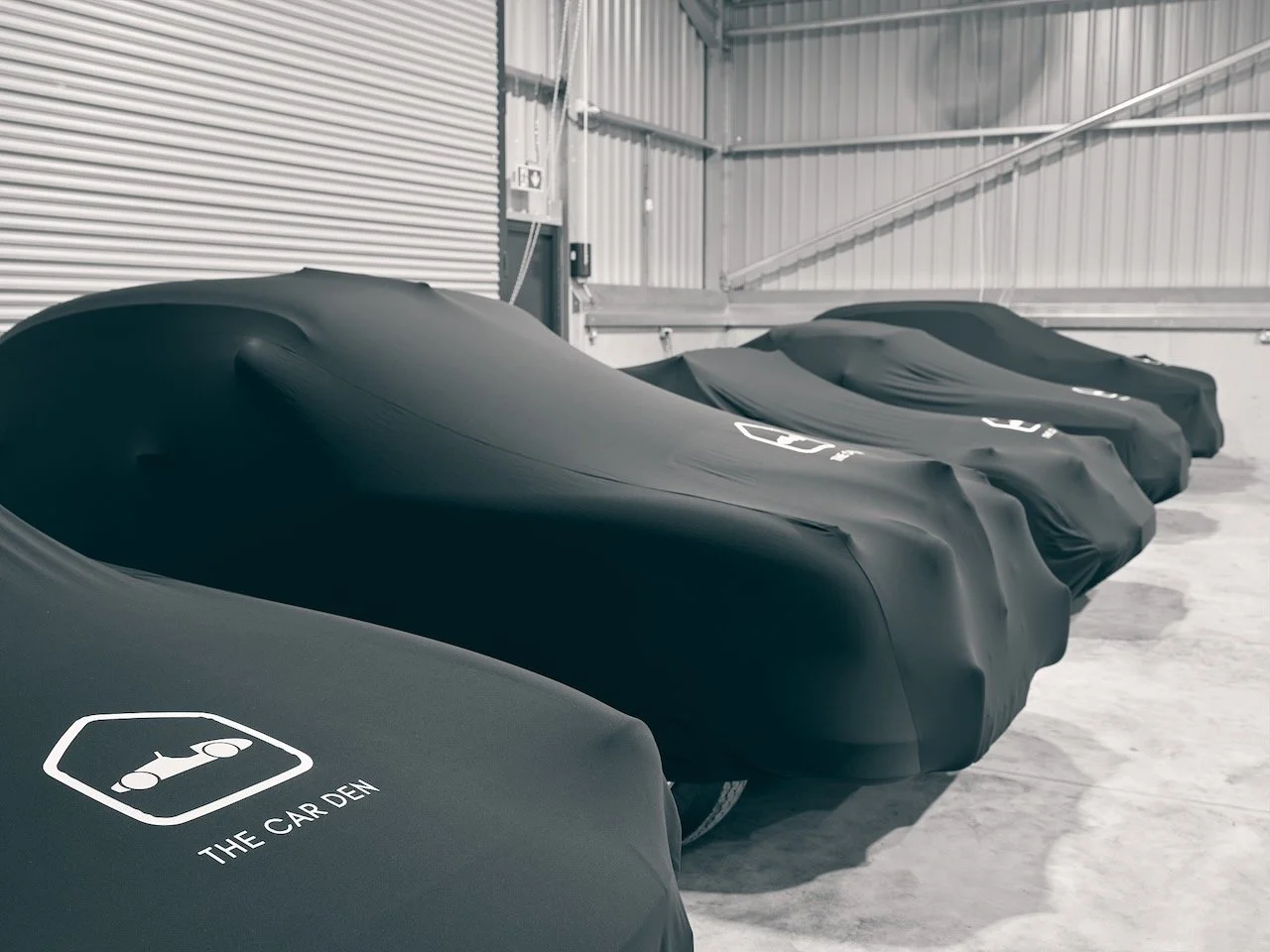 Row of classic cars under branded The Car Den covers in Standard Indoor storage
