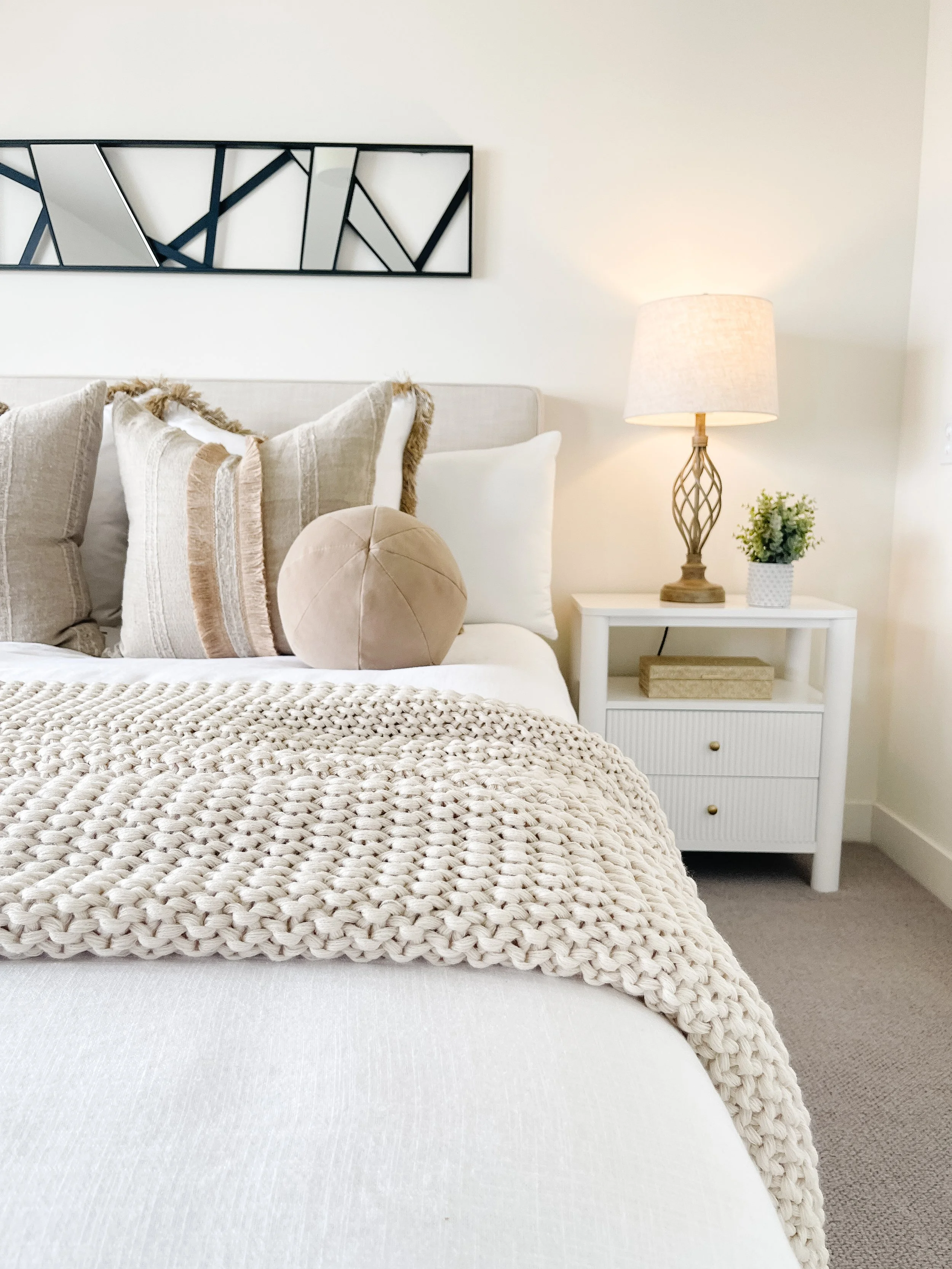 Staged primary bedroom in a Camano Island house featuring a neutral upholstered bed, layered bedding, and soft lighting.