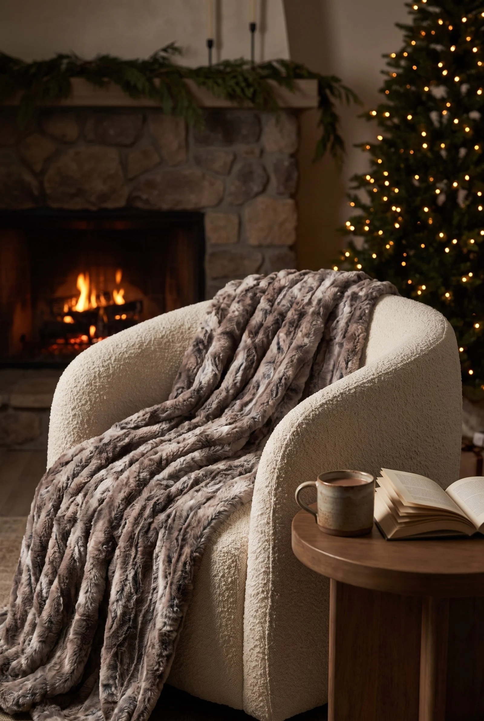 Driftwood faux fur throw draped over a cream boucle armchair beside a lit stone fireplace with cedar garland on the mantel.