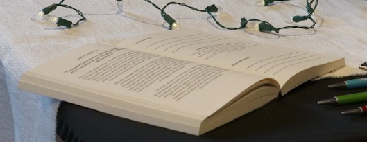 Open book with text, illuminated string lights, and pens on a table