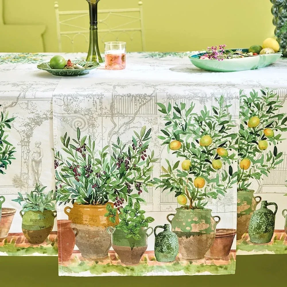 Table runner with potted lemon, olive and other plants, sitting on decorated table with matching tablecloth.