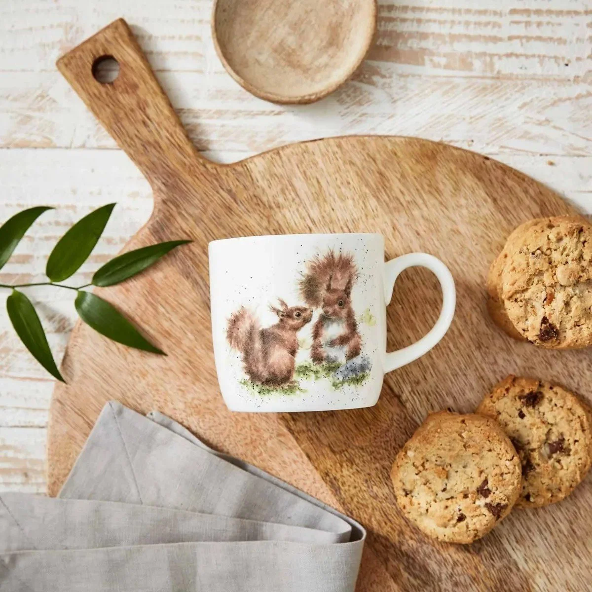 Squirrel mug laying flat on wood kitchen piece near cookies.