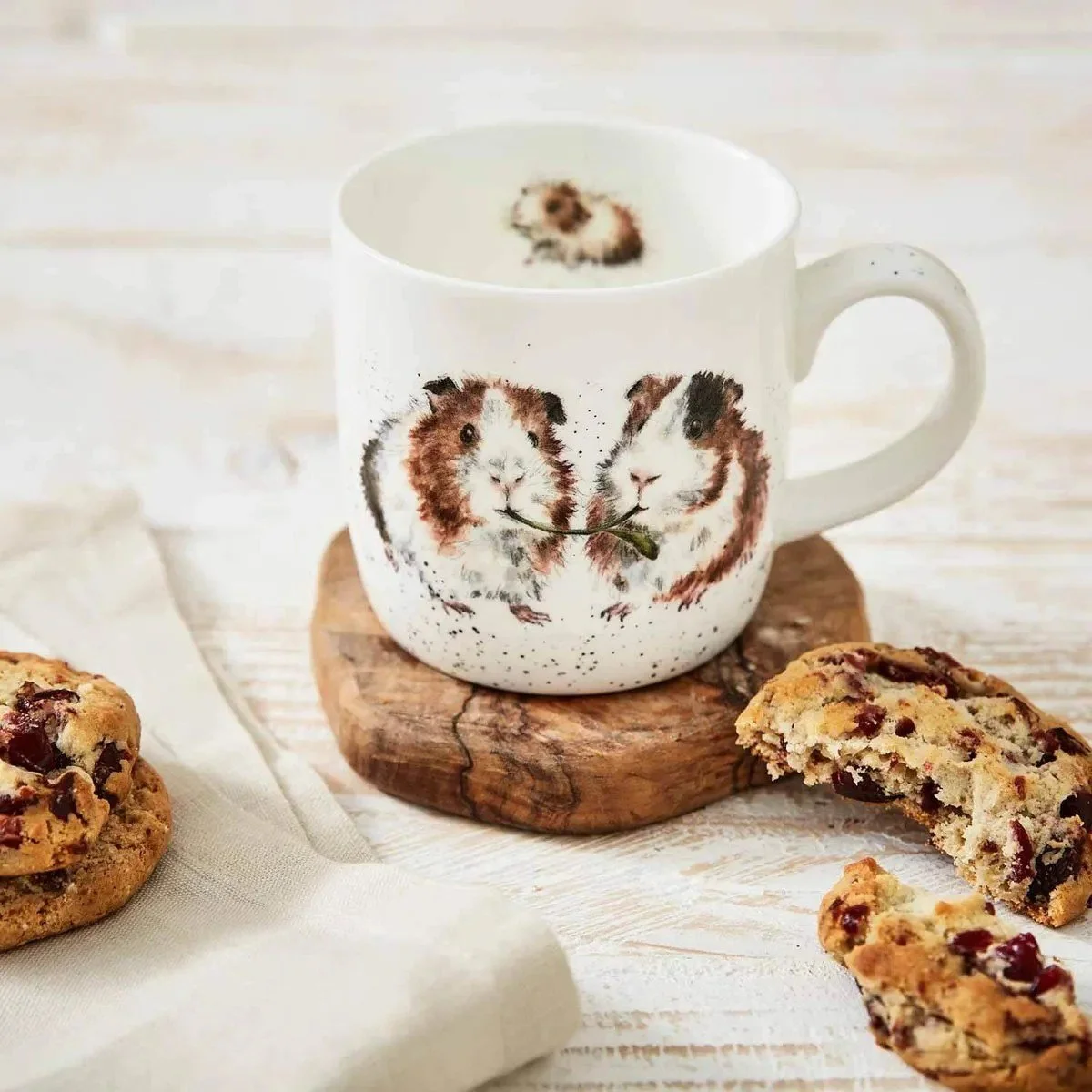 Guinea pig mug on wood coaster beside chocolate chip cookies.