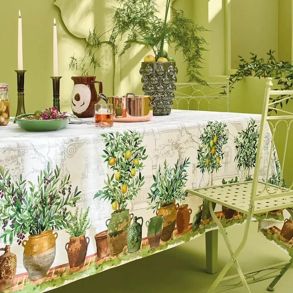 Cream tablecloth with large potted plants, including olives and lemon plants, running along each side, on table with other decor.