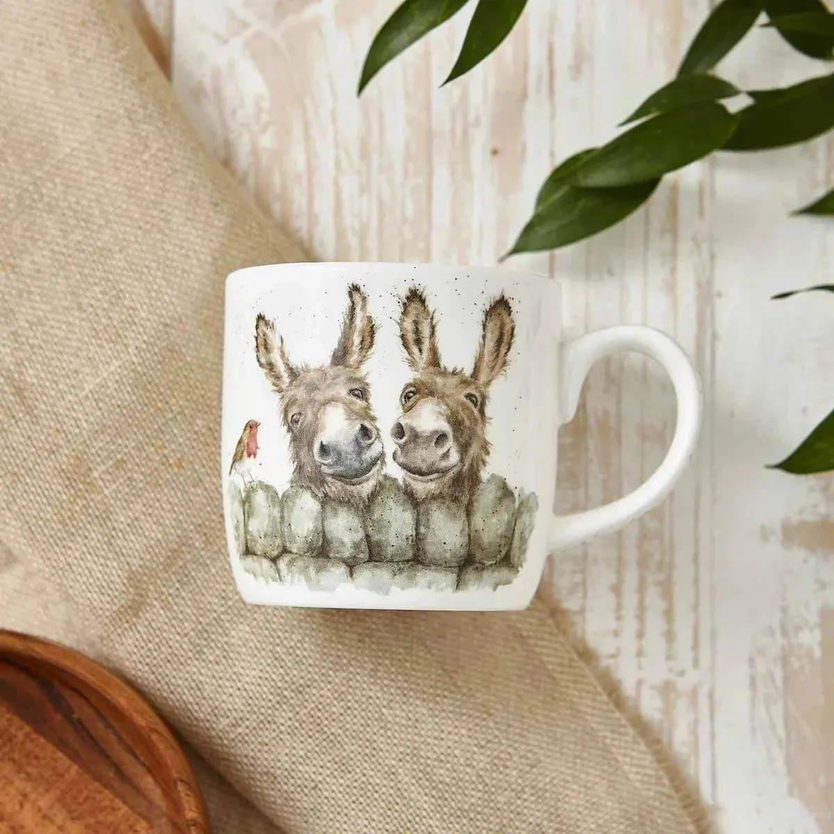 Empty white mug with two donkeys laying flat on linen.