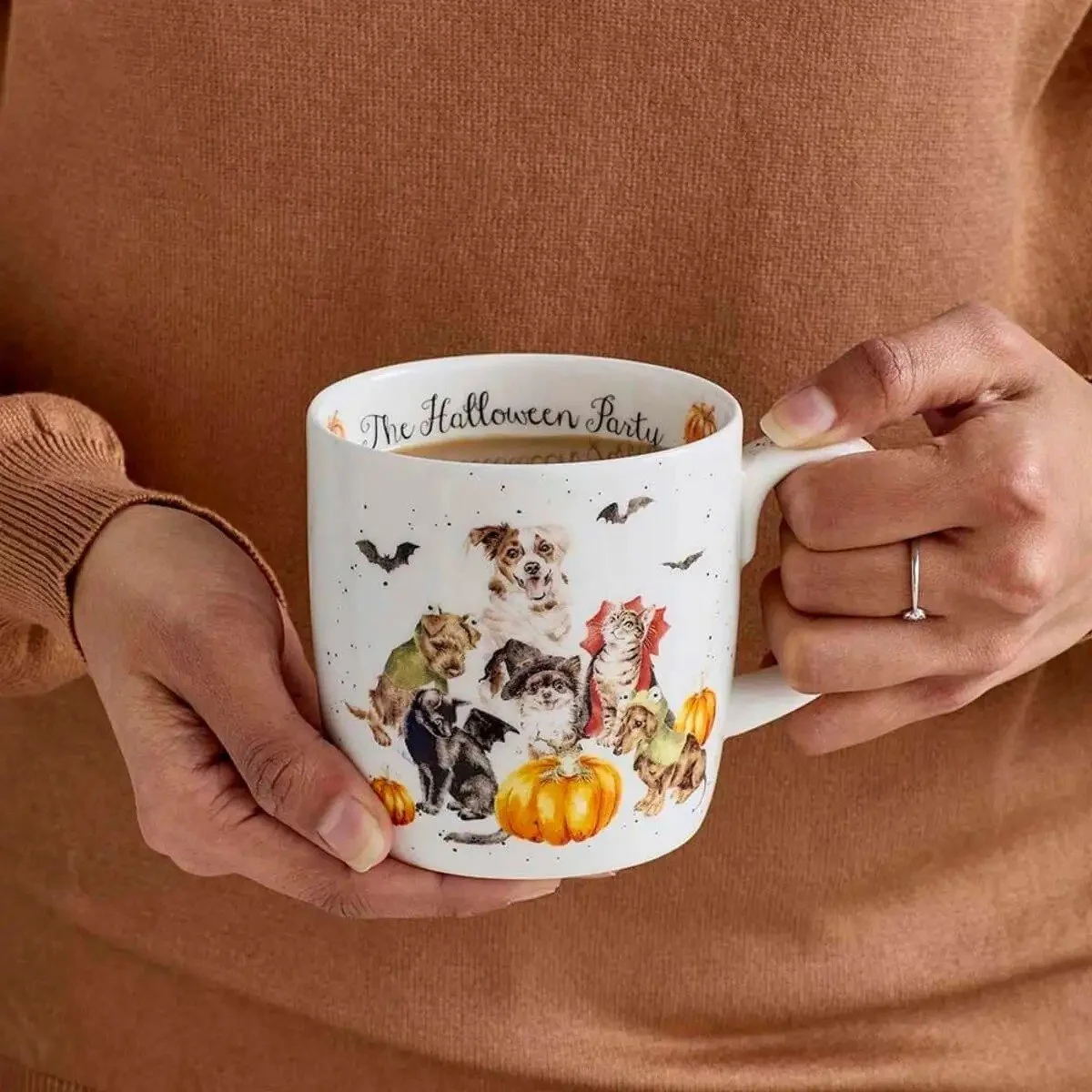 woman holding mug with dogs and cats in Halloween costumes.