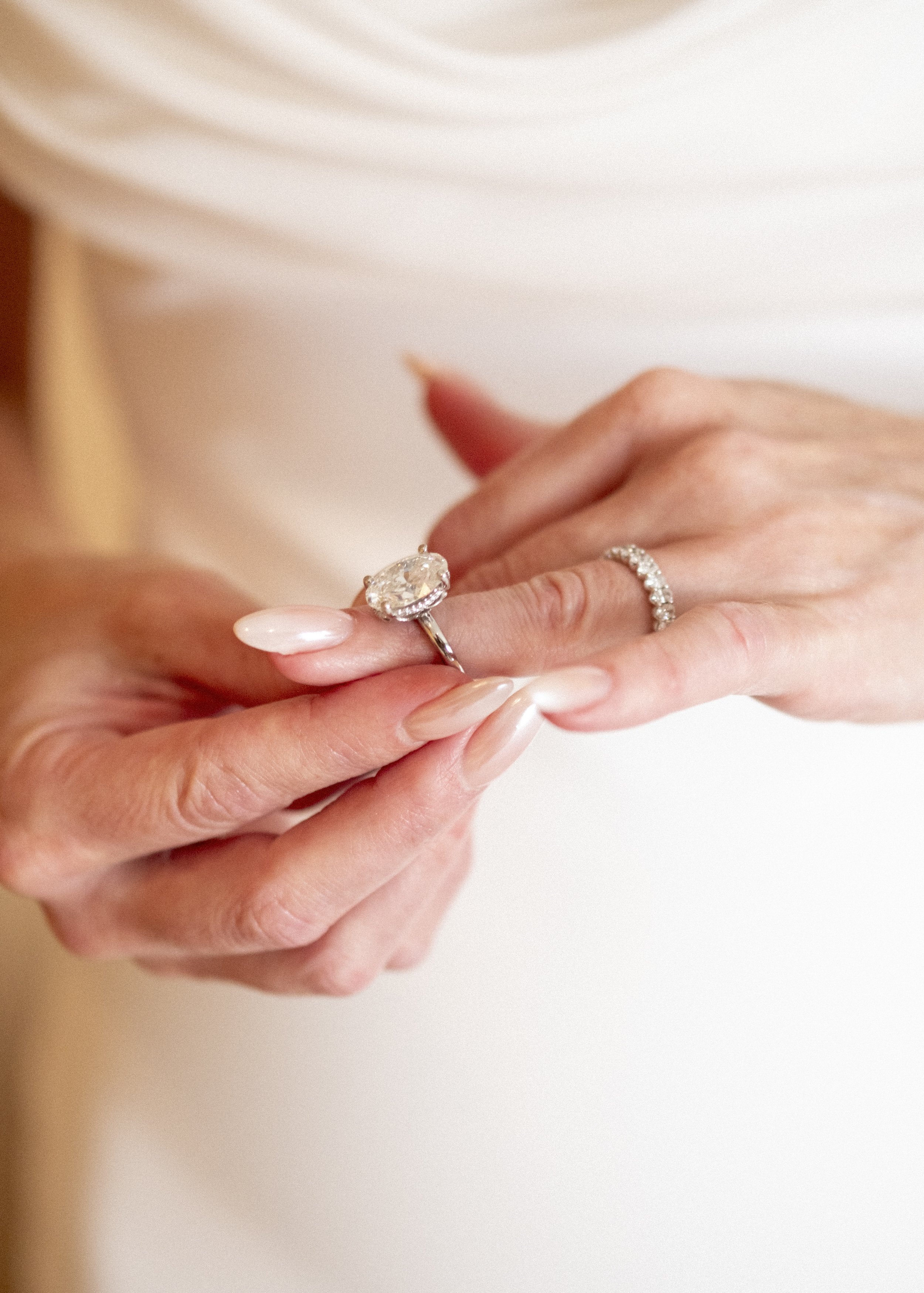 Close-up of a person wearing diamond rings on both hands, holding a large oval engagement ring with a diamond center stone.