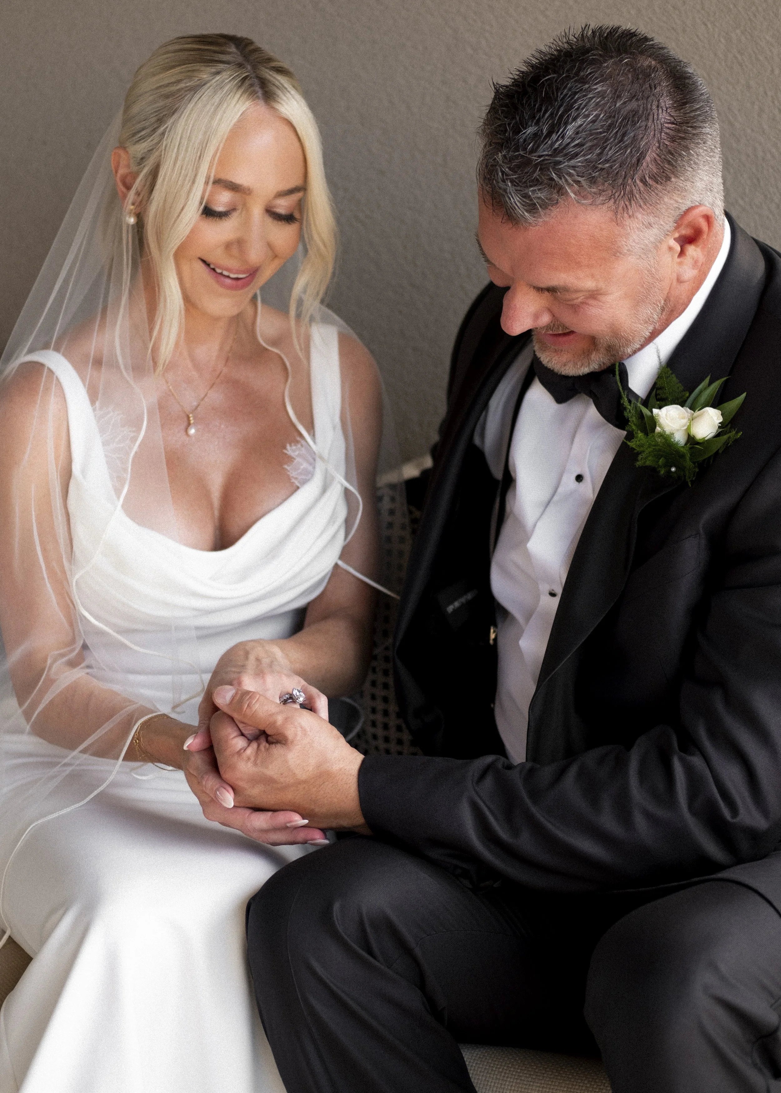 A bride and groom sit close together, holding hands, smiling joyfully during their wedding ceremony.
