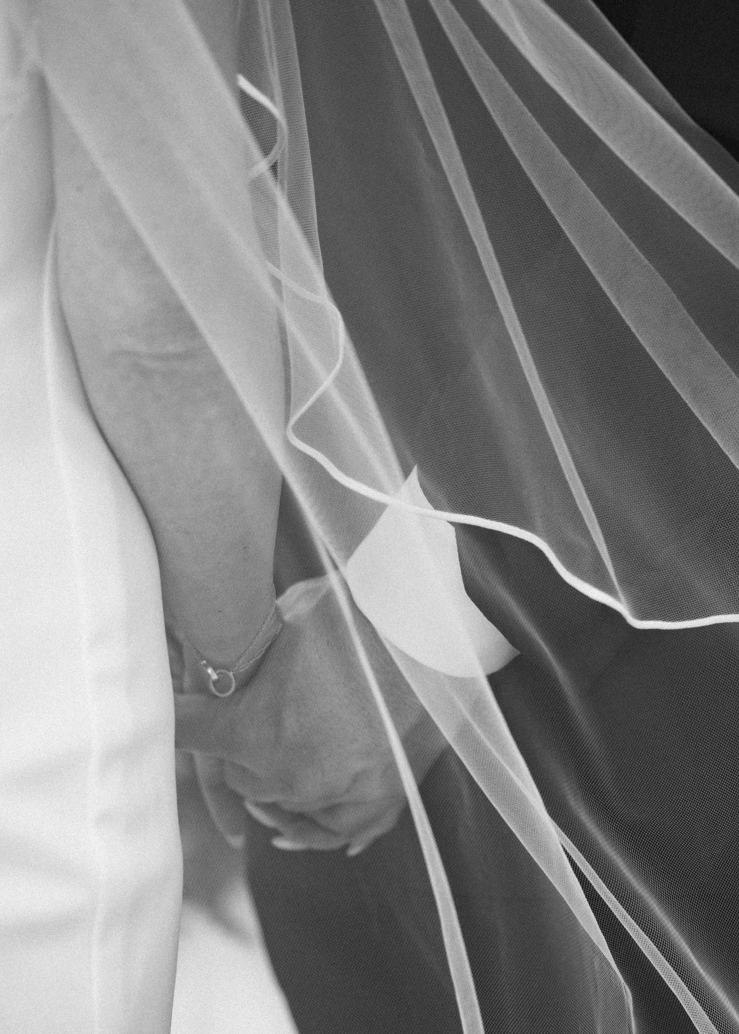 Close-up of a wedding veil with tulle fabric and a decorative flower, partially covering a person's hand.