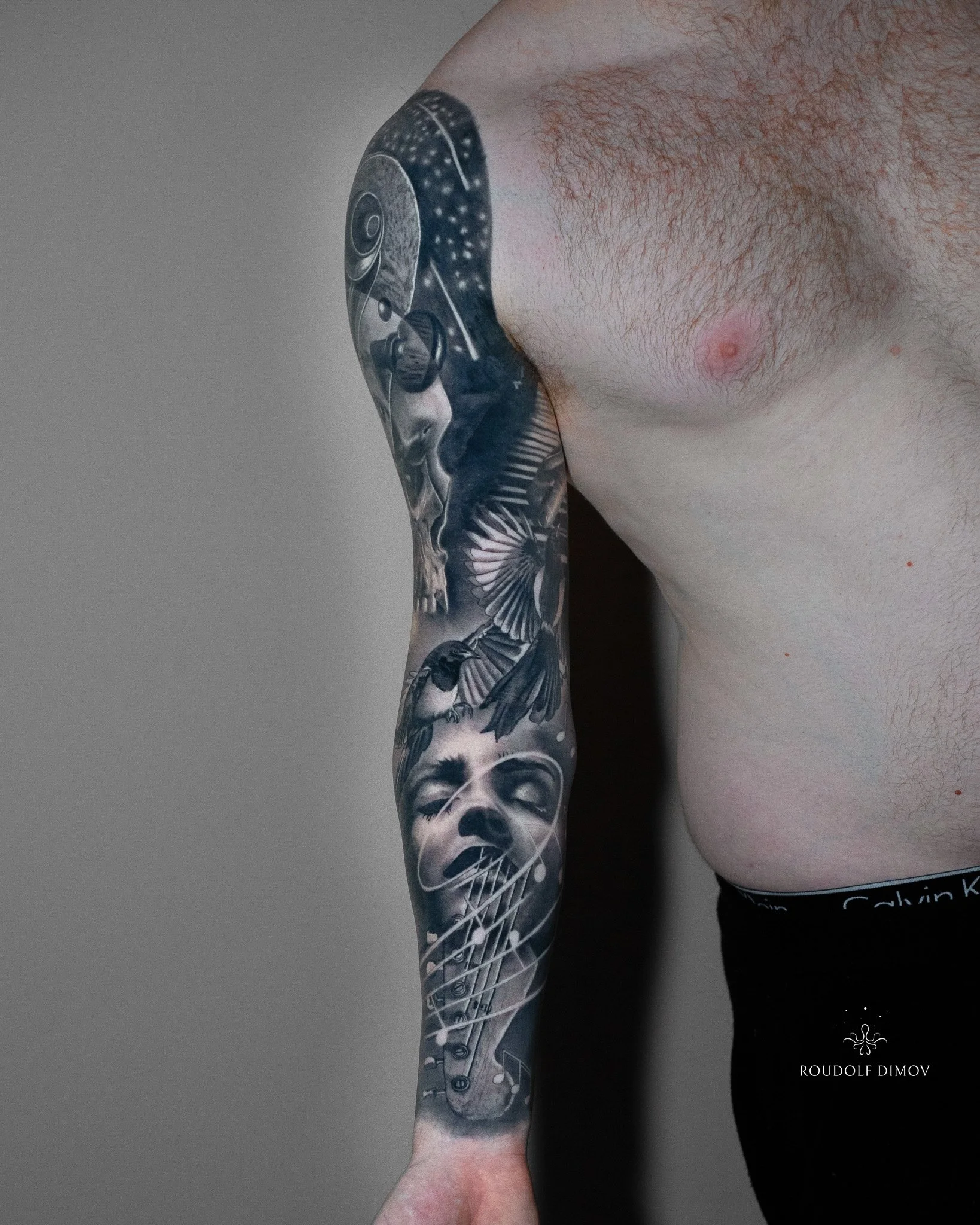 Black and grey realism full sleeve tattoo featuring a female face, musical notes, two magpies, and seamless transitions into cosmic elements, created by London tattoo artist Roudolf Dimov.