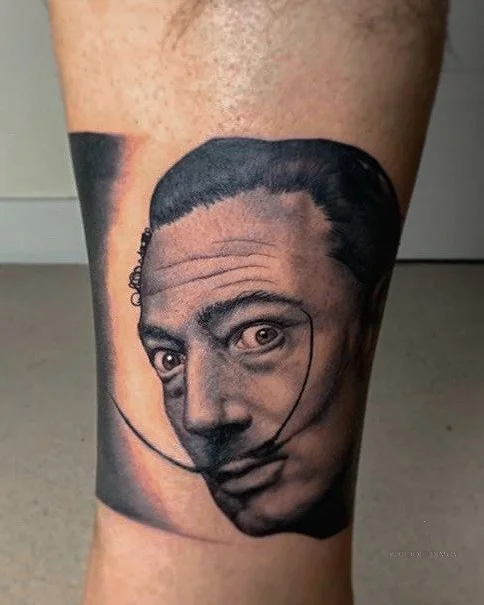 Black & grey realism portrait of Salvador Dalí tattooed on the calf, showcasing fine detail and smooth shading. Tattoo by Roudolf Dimov in London.