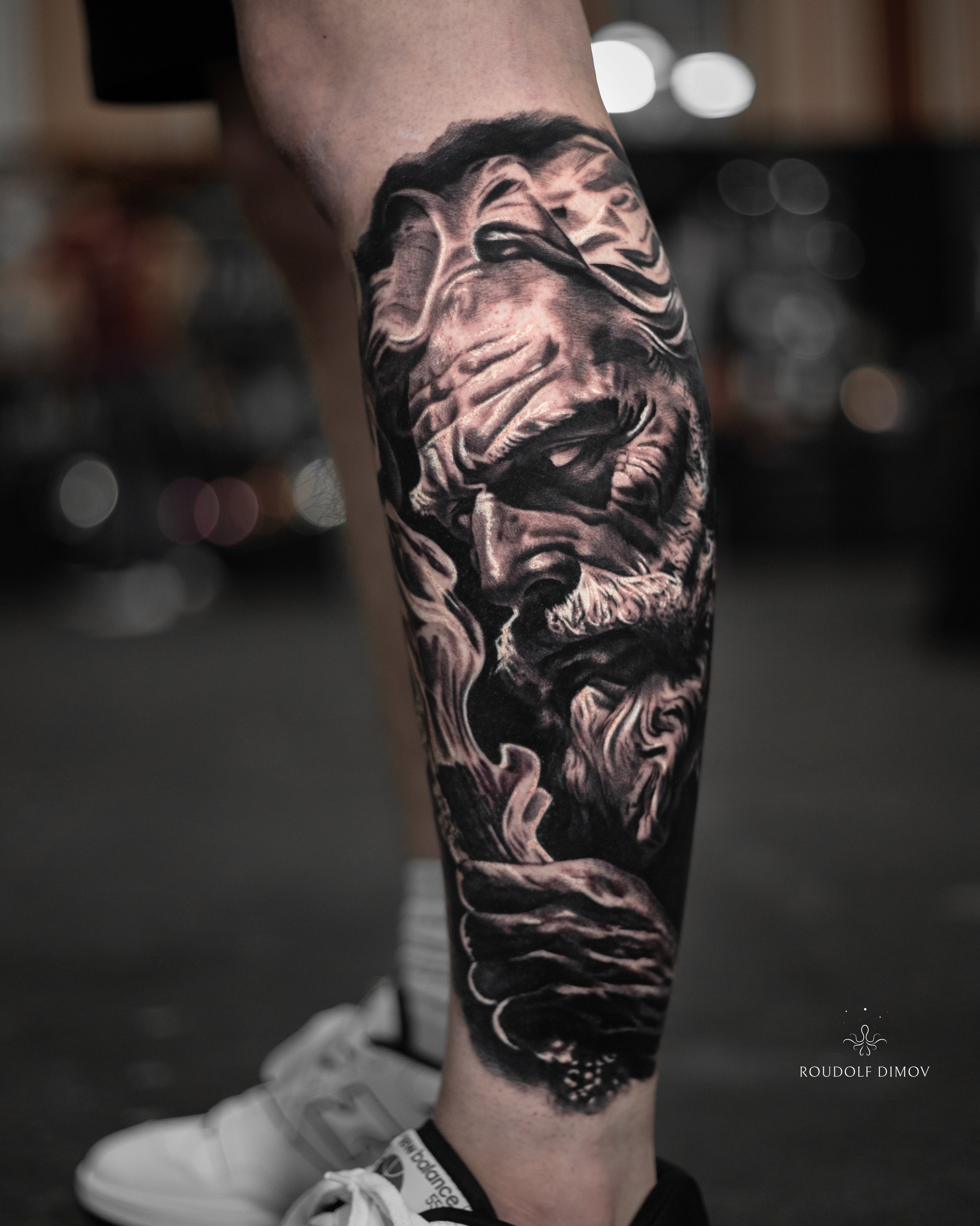 Hades tattoo on the lower leg in black and grey realism, featuring detailed Greek mythology elements. Tattoo artist Roudolf Dimov, London.