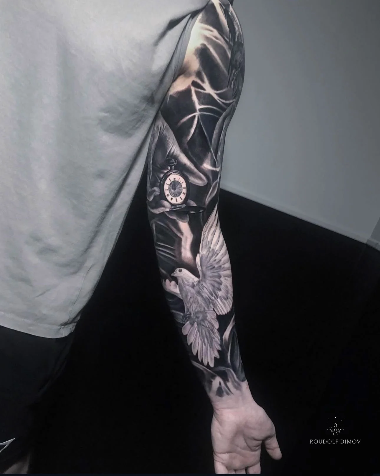 Dove and pocket watch tattoo on the inner forearm as part of a full sleeve in black and grey realism, featuring soft transitions and symbolic imagery. Tattoo artist Roudolf Dimov, London.