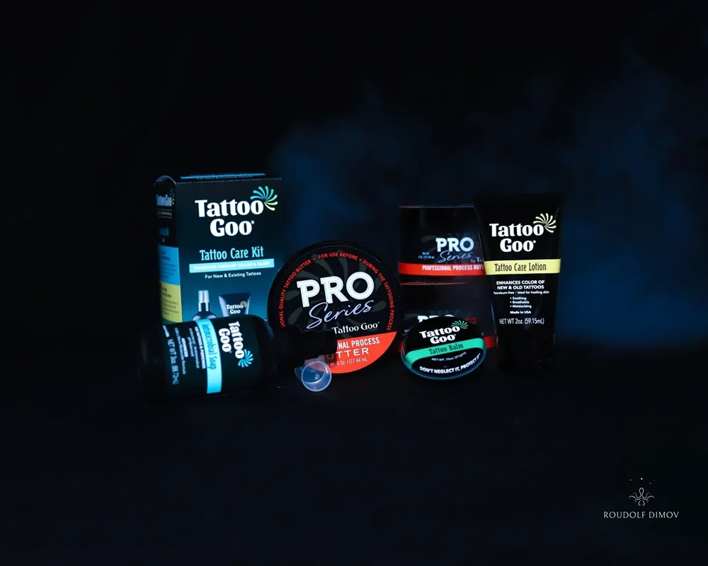Tattoo Goo tattoo care products including a tattoo care kit, tattoo balm, tattoo lotion, and professional process bottle, all arranged on a black background.