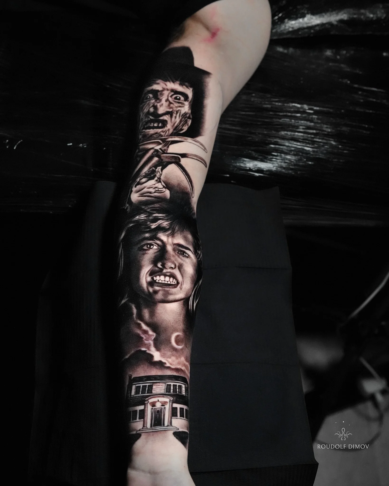 Freddy Krueger horror tattoo on the forearm in black and grey realism, featuring detailed portrait work, iconic glove blades, and atmospheric background elements. Tattoo artist Roudolf Dimov, London.