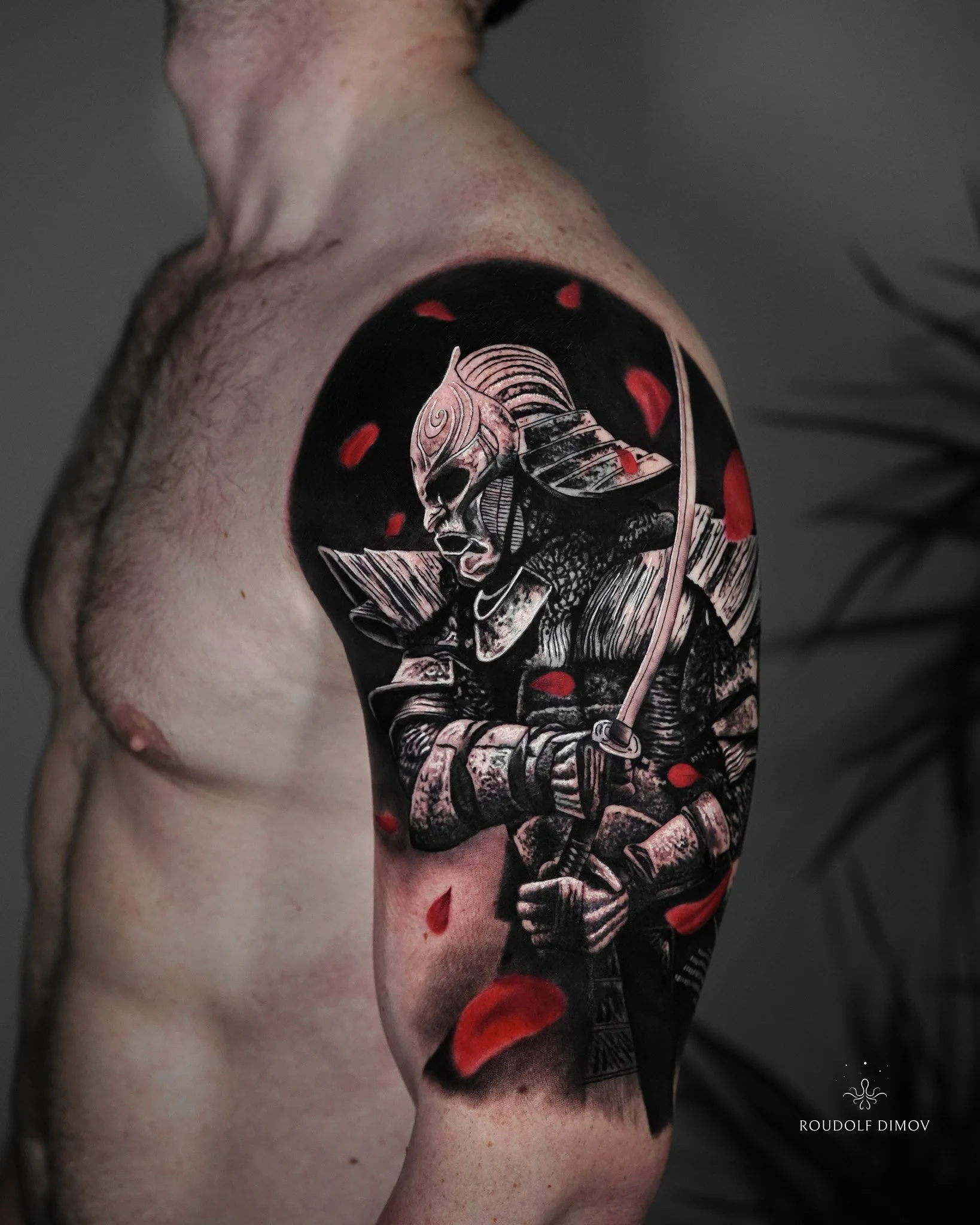 Samurai warrior tattoo on the shoulder in black and grey realism with red accent details, featuring armour, katana, and dynamic composition. Tattoo artist Roudolf Dimov, London.