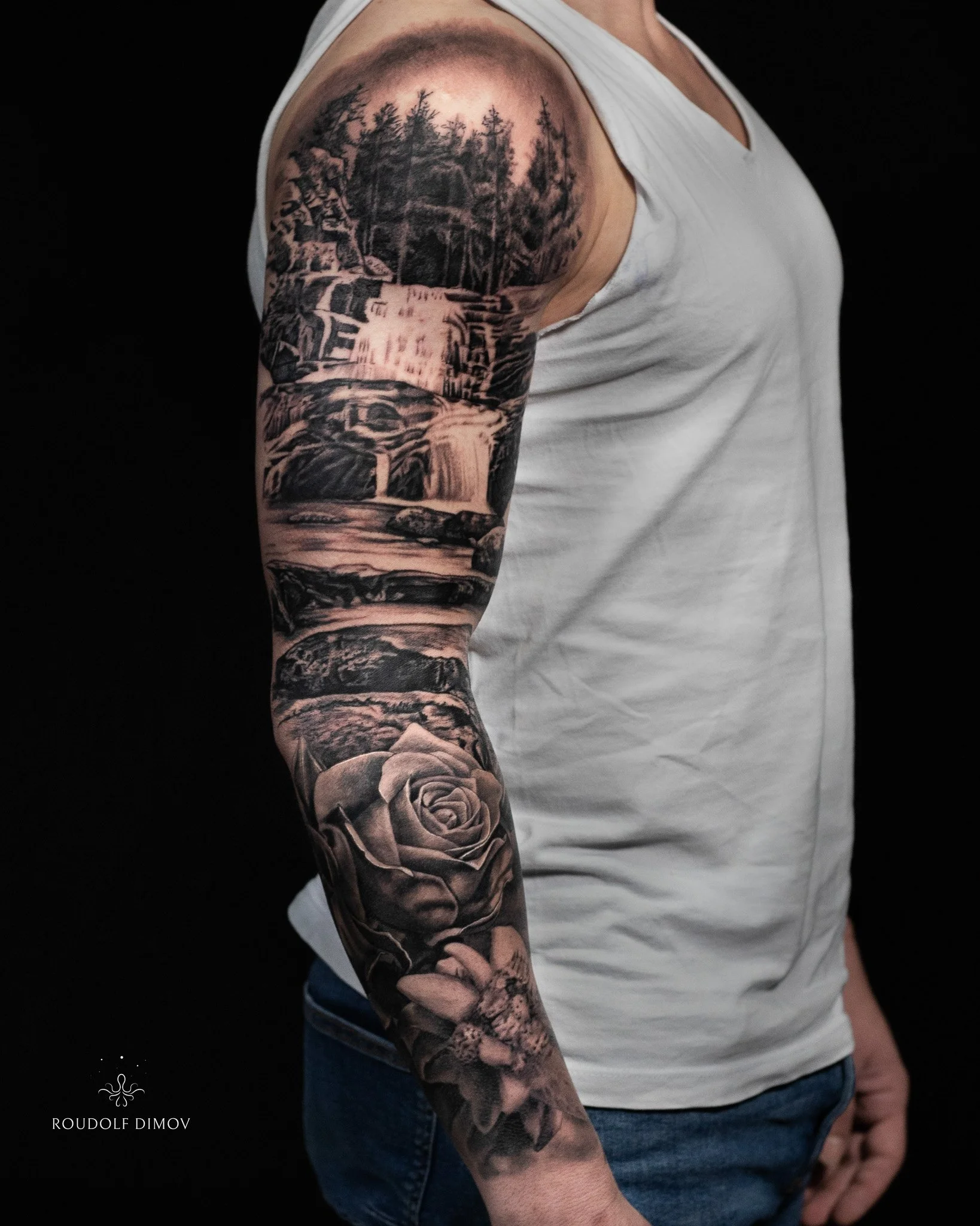 Black & grey realism full sleeve featuring a waterfall and forest landscape, Bulgarian rose, and edelweiss on the arm. Tattoo by Roudolf Dimov in London.