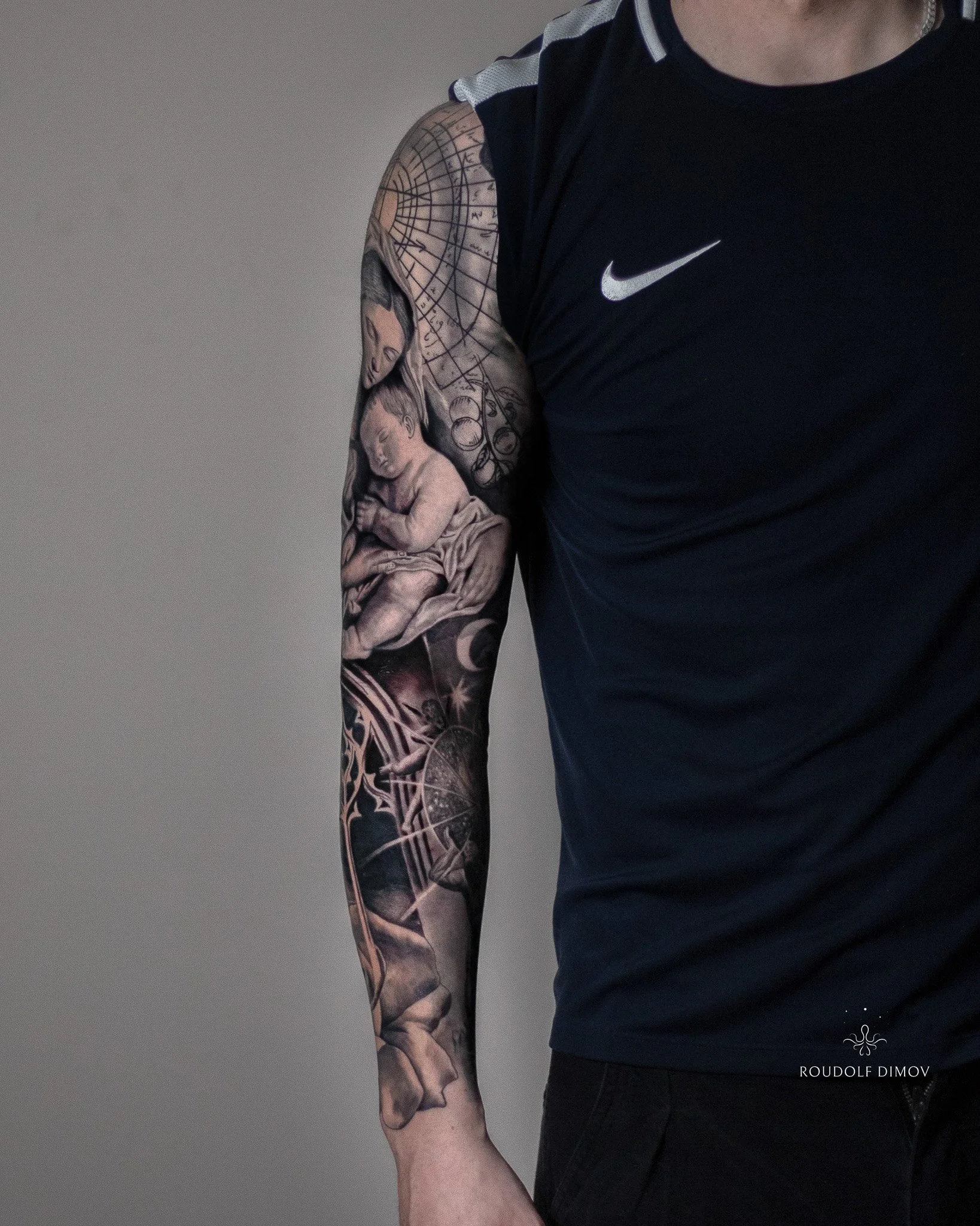 Full black and grey realism sleeve featuring the Virgin Mary and baby Jesus, Renaissance sketchwork, and lower-arm details blending into the forearm.