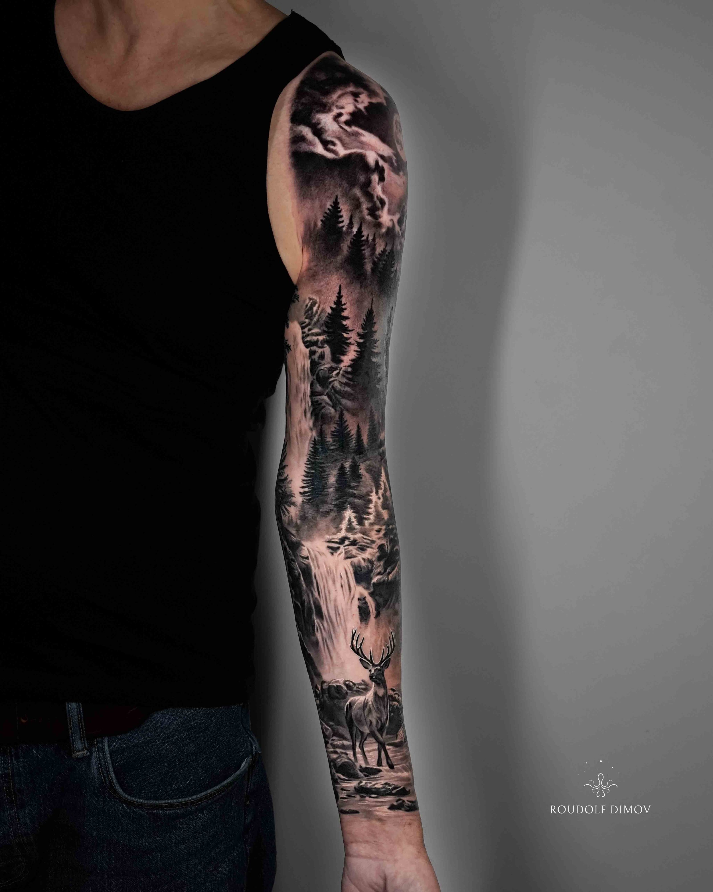 Black and grey realism nature sleeve tattoo featuring a waterfall, forest landscape, and stag deer by London tattoo artist Roudolf Dimov. This full sleeve tattoo combines wilderness scenery with detailed realism, creating a flowing composition inspir