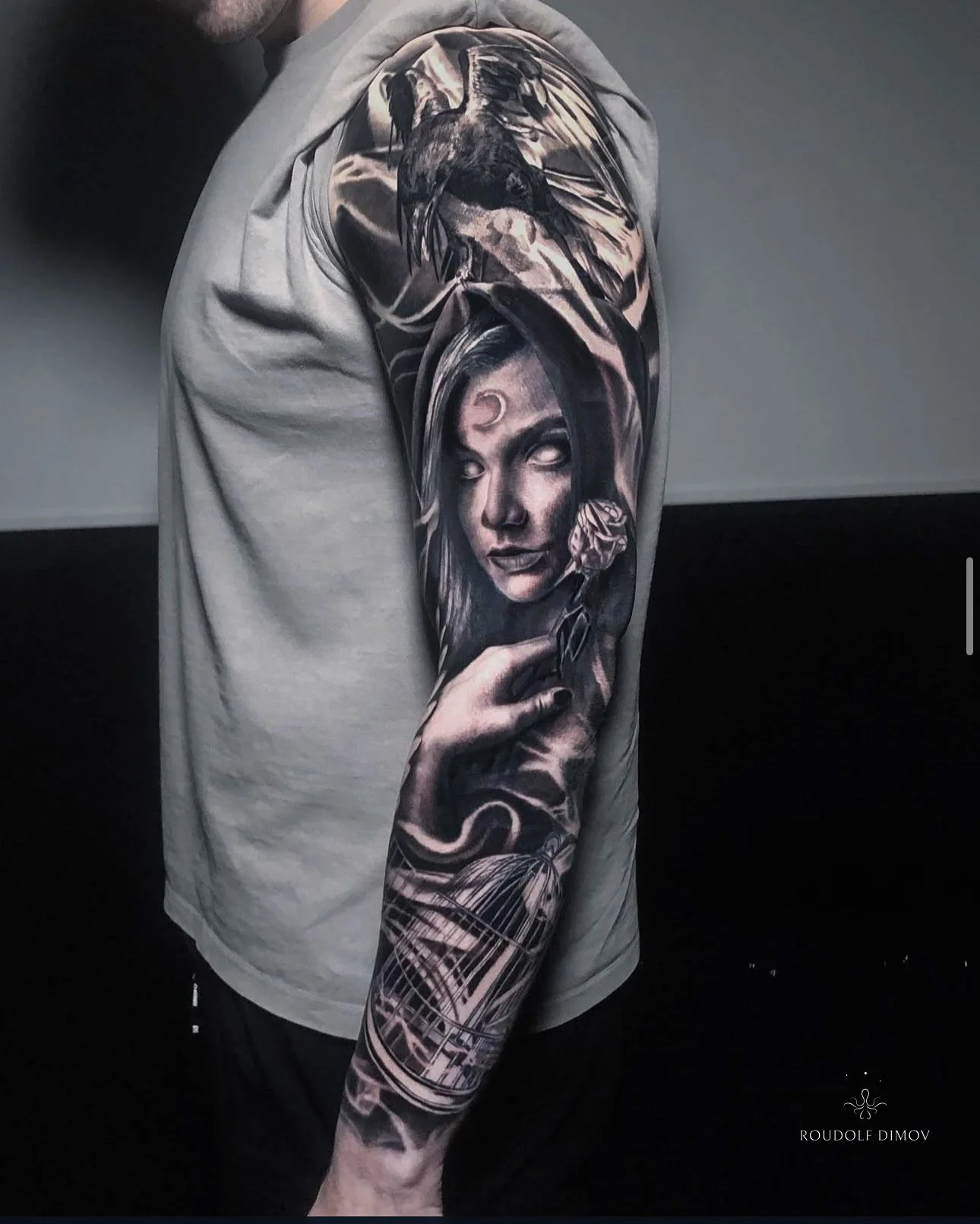 Raven and witch portrait full sleeve tattoo in black and grey realism, featuring detailed textures, mystical elements, and flowing composition along the arm. Tattoo artist Roudolf Dimov, London.