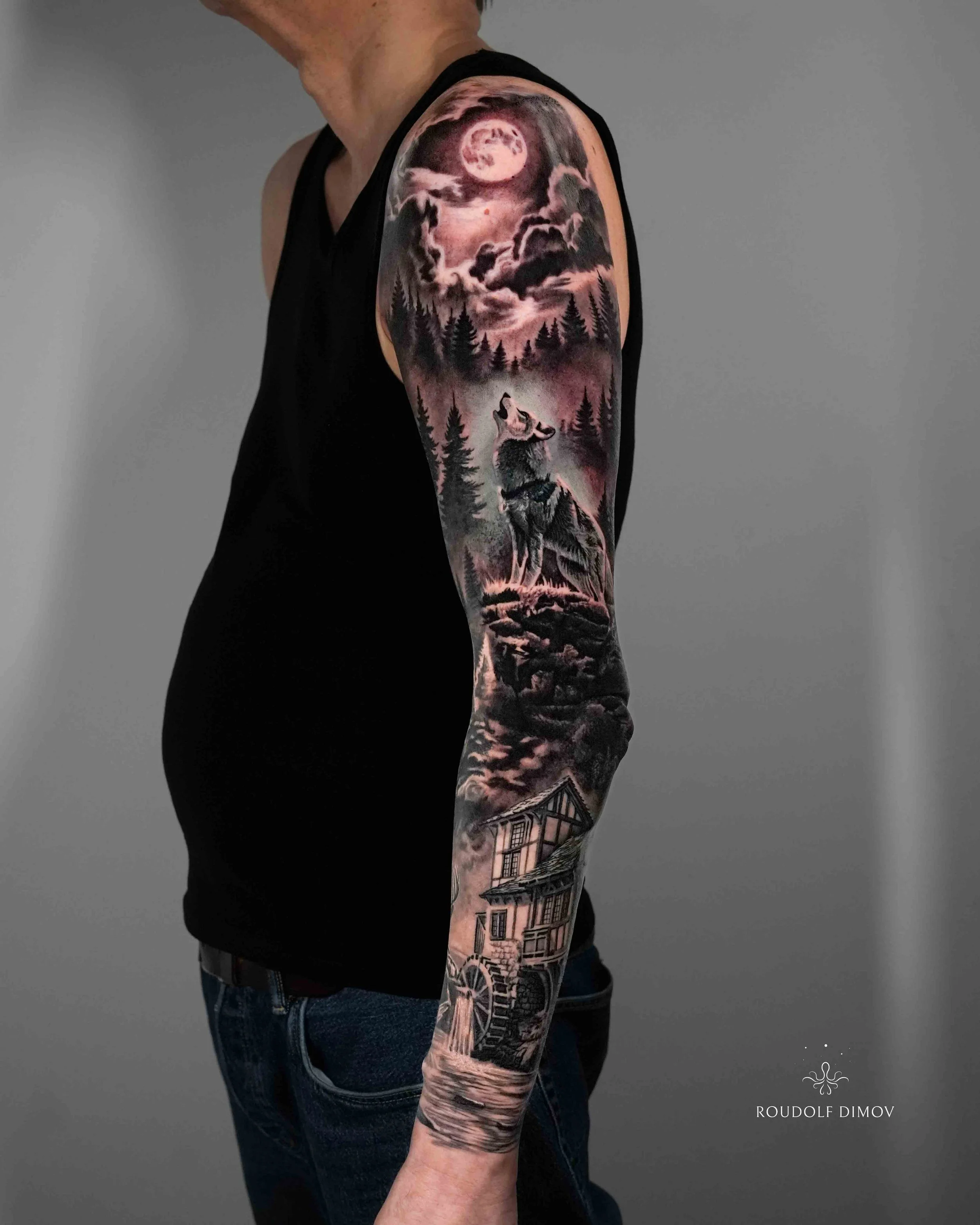 Black and grey realism wolf sleeve tattoo featuring a howling wolf, full moon, dark forest, and detailed house scene by London tattoo artist Roudolf Dimov. This full arm tattoo combines nature, wilderness, and atmospheric realism to create a cinemati
