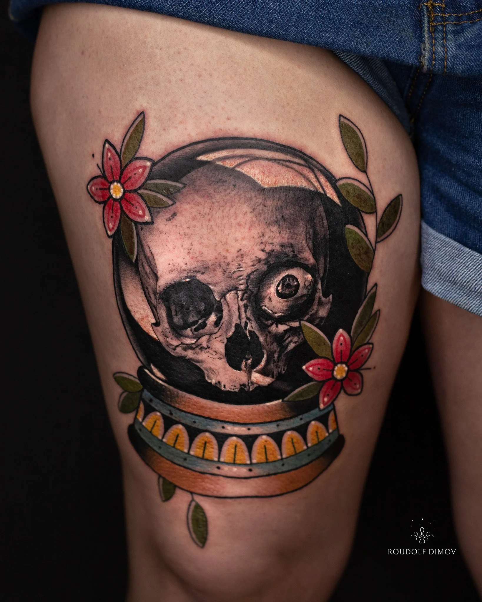 Neotraditional skull inside a crystal ball tattoo on the thigh, featuring bold colours and floral elements. Tattoo by Roudolf Dimov in London.
