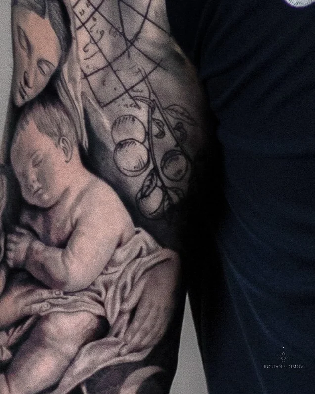 Black and grey realism tattoo of baby Jesus with Renaissance-style sketchwork and subtle peach drawings on the upper arm.