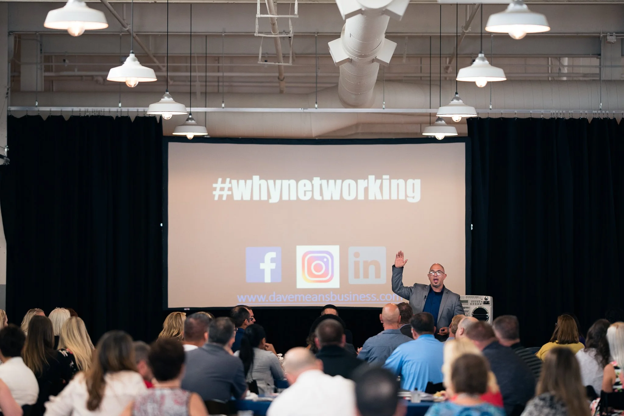 A speaker giving a presentation titled '#whynetworking' on a large screen, in front of an audience in a conference room.