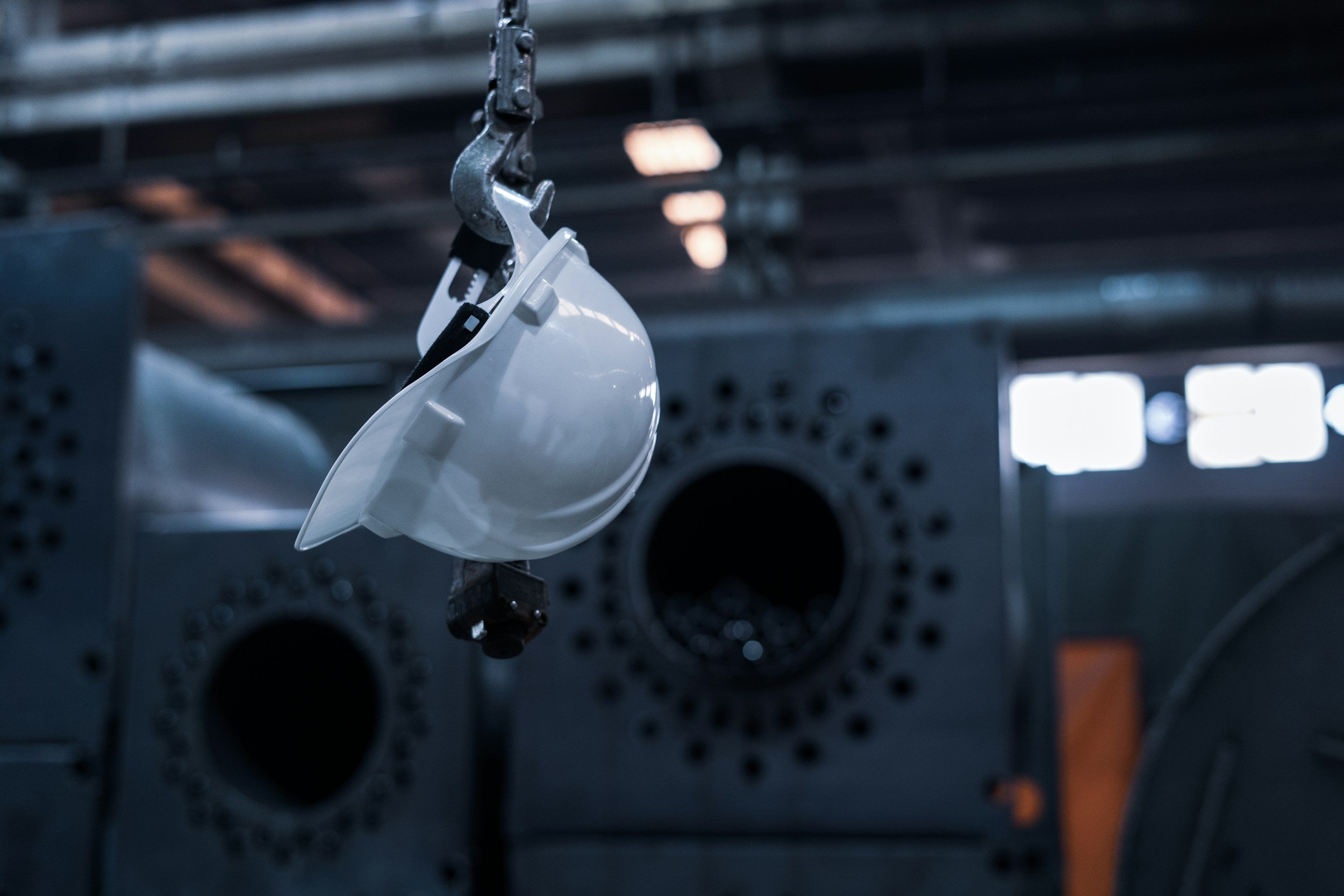 A white face shield is hanging from a metal hook in an industrial or laboratory setting with a perforated metal background.