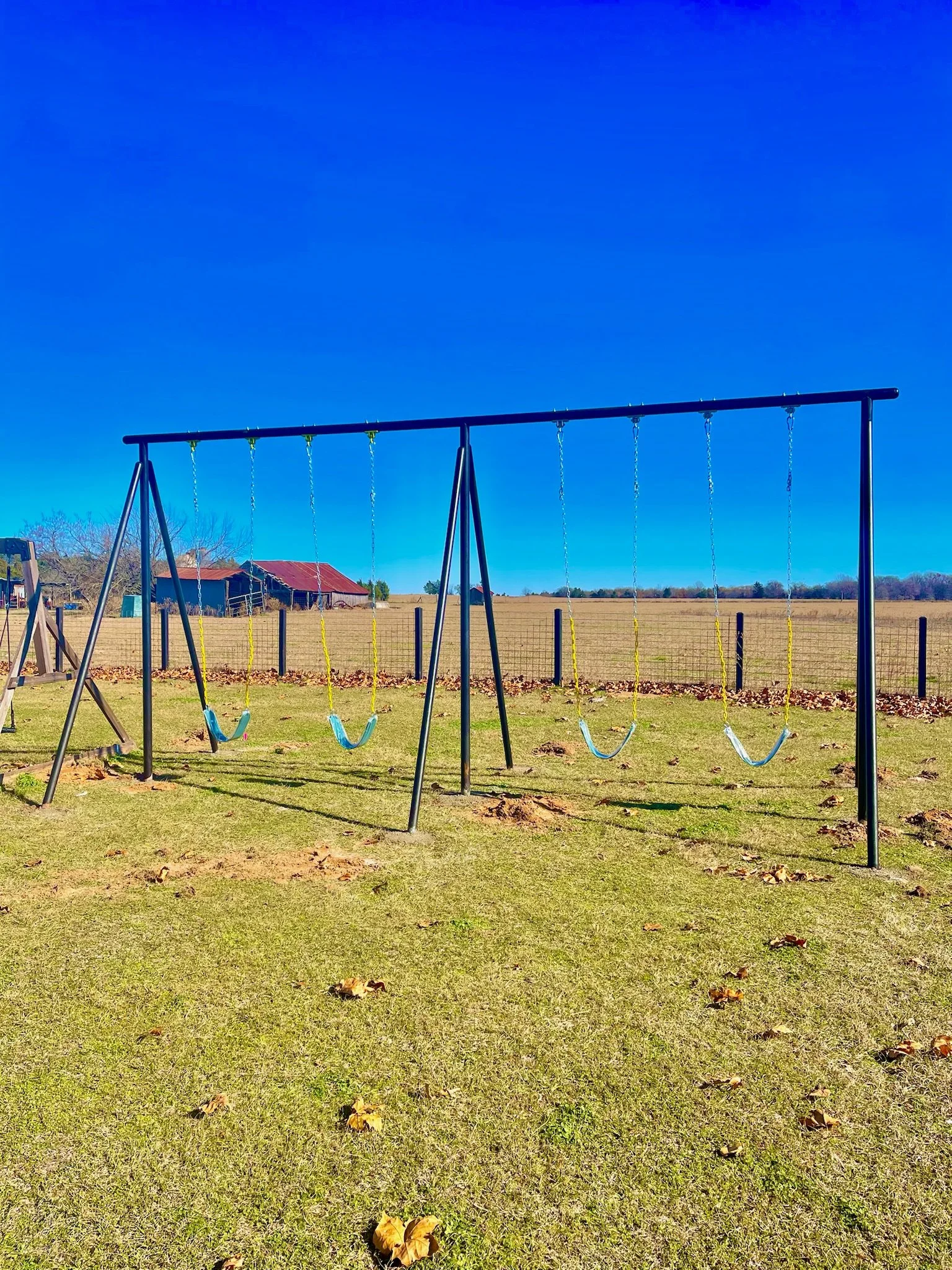 Empty swing set with six swings on a grassy field under a clear blue sky.