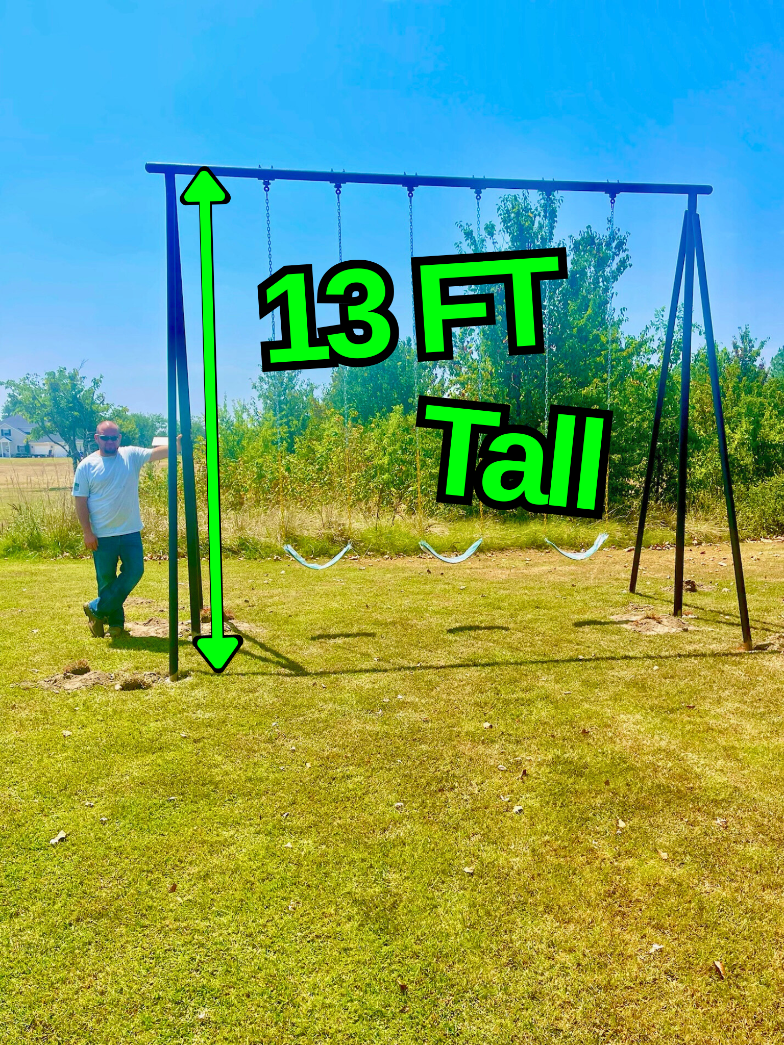 An outdoor swing set with three swings on a grassy field. A man stands next to the left side of the swing set, wearing sunglasses, a white t-shirt, and blue jeans. The swing set is 13 feet tall, as indicated by green labeled text and arrows.
