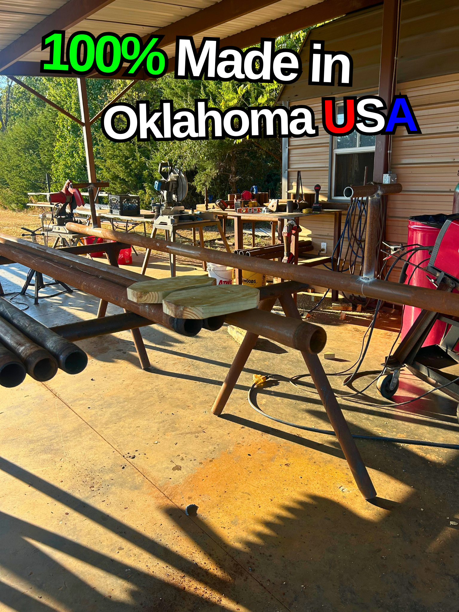 Outdoor workshop with tools and wooden pipes, under a metal roof, with trees in the background. Text overlay reading '100% Made in Oklahoma USA' in colorful letters.