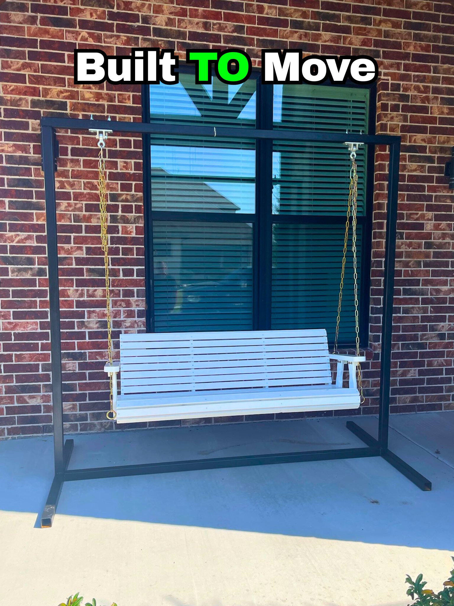A porch swing with a black metal frame and a white slatted seat and back is hanging from chains on a brick wall background. Text overlay says 'Built TO Move' with 'TO' in bright green.