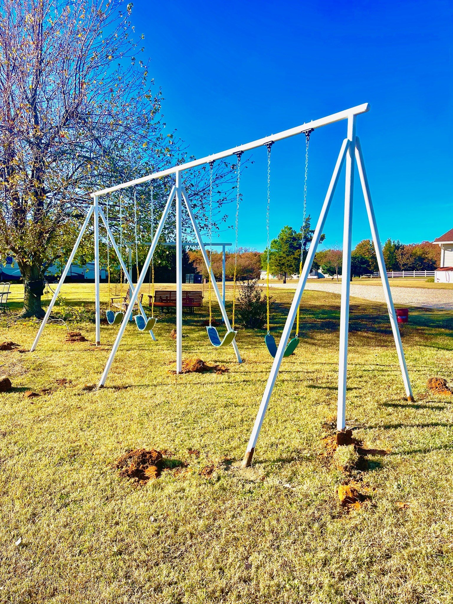 Colorful outdoor swingset on grassy field with trees and houses in the background, under a bright blue sky.