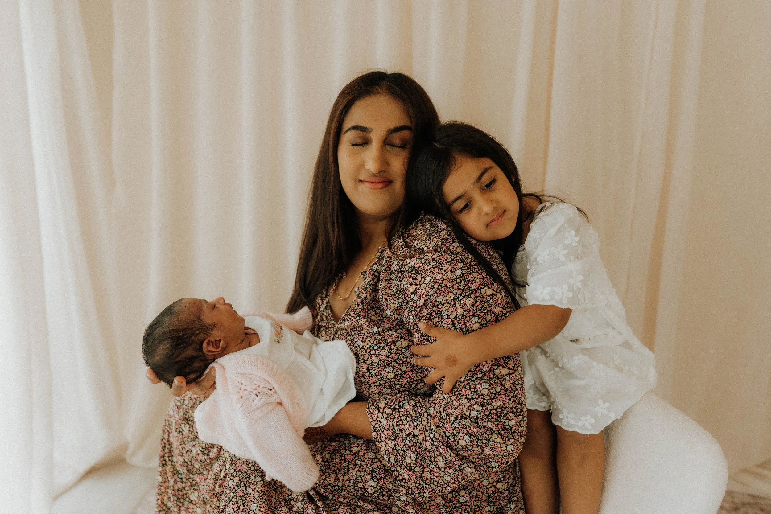 Image of a mother with her newborn daughter and toddler daughter on their motherhood shoot in Didsbury Family Photography Studio
