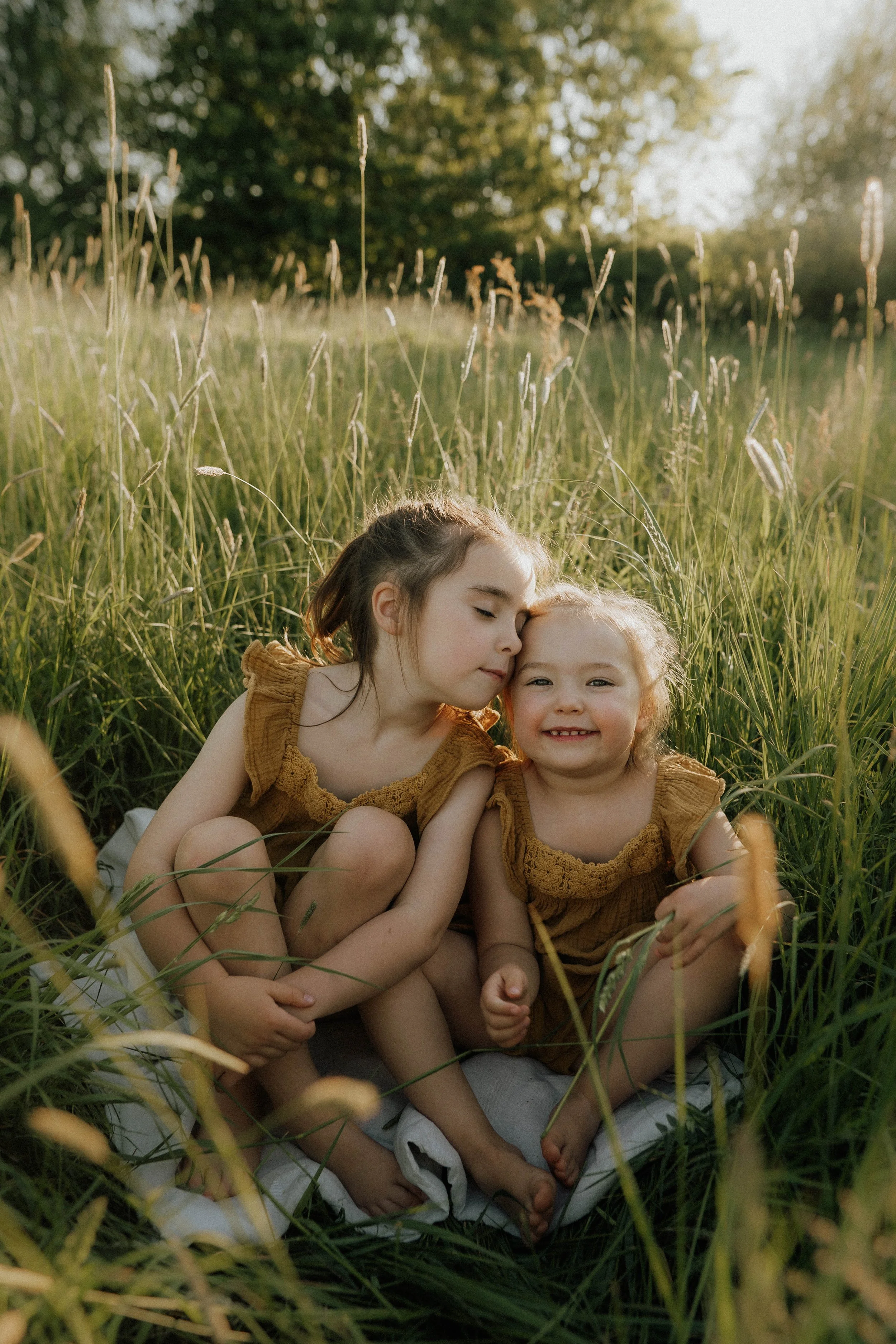 Image of two sisters cuddling up in a meadow on their family shoot with Didsbury family photographer Copper + Olive Photo