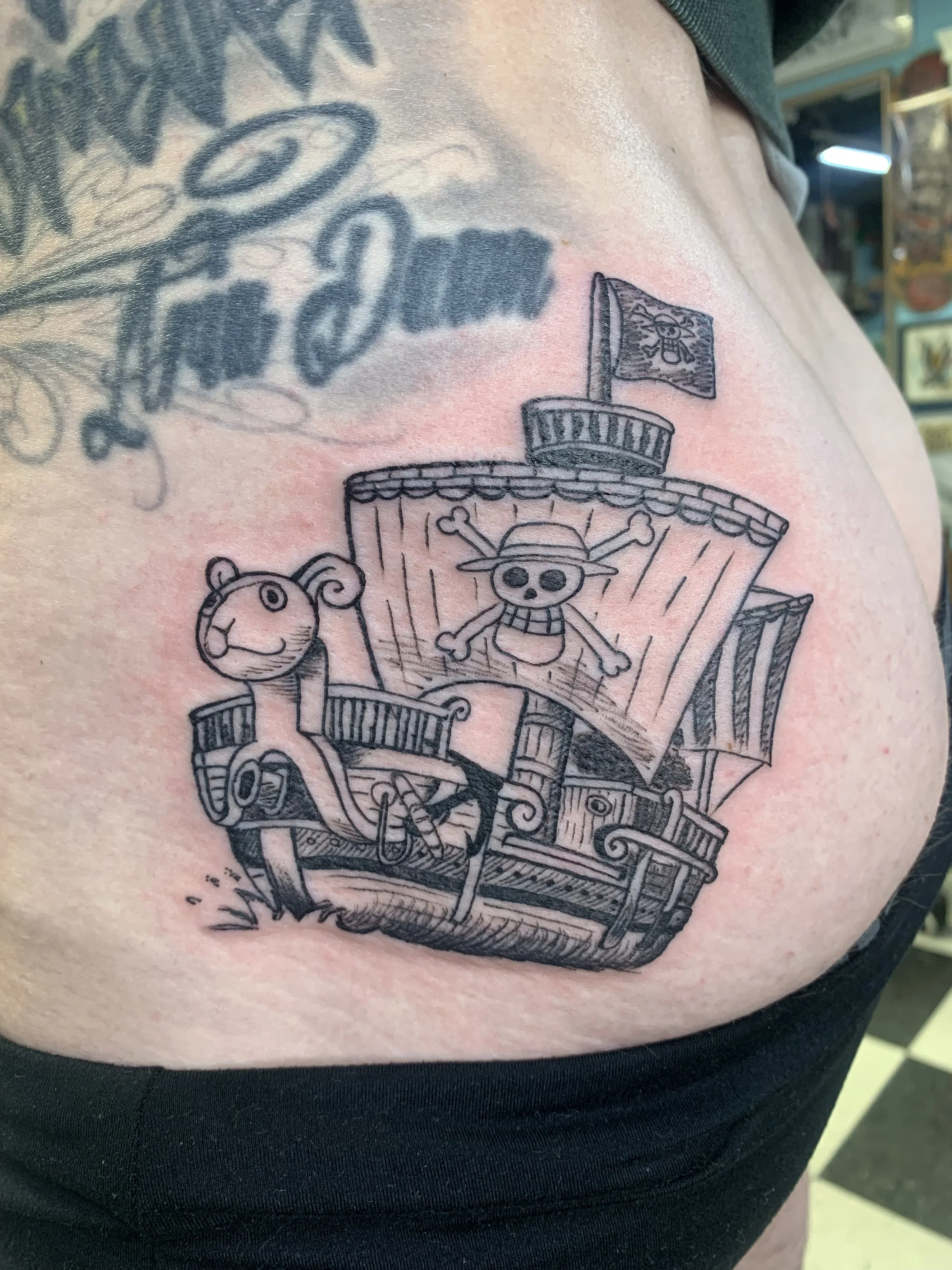 Tattoo of a treasure chest with a skeleton wearing a hat and crossbones, a lion, and a flag with a skull and crossbones, on a person's upper chest.