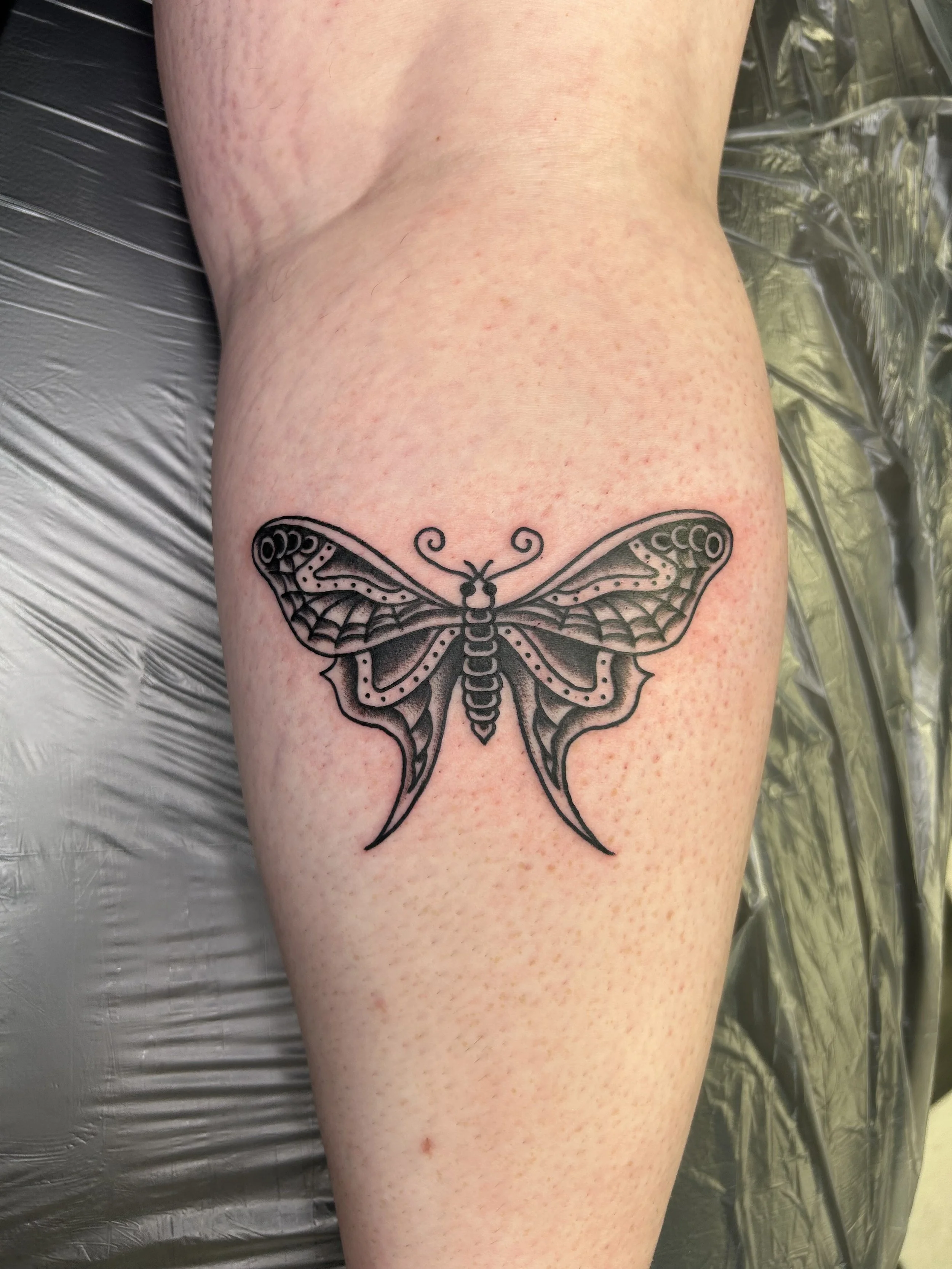 Black line art tattoo of a butterfly on a person's upper thigh, with detailed wings and body.