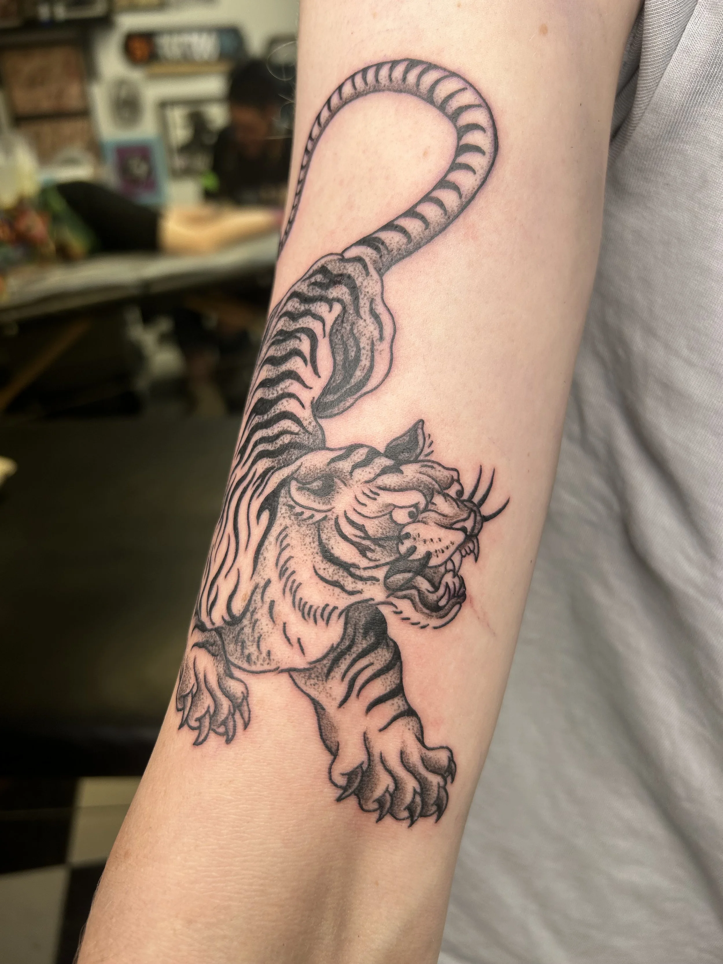 A black and gray tattoo of a lion's head on a person's arm, with the lion's mane flowing around.