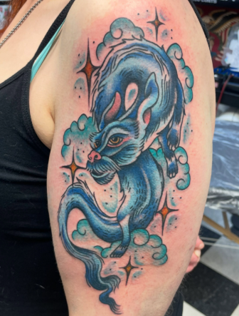 Blue dragon tattoo on upper arm, surrounded by clouds and stars.