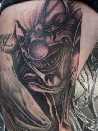 Close-up of a black and gray clown tattoo on someone's side, depicting a clown with a big nose, wide smile, and detailed shading.